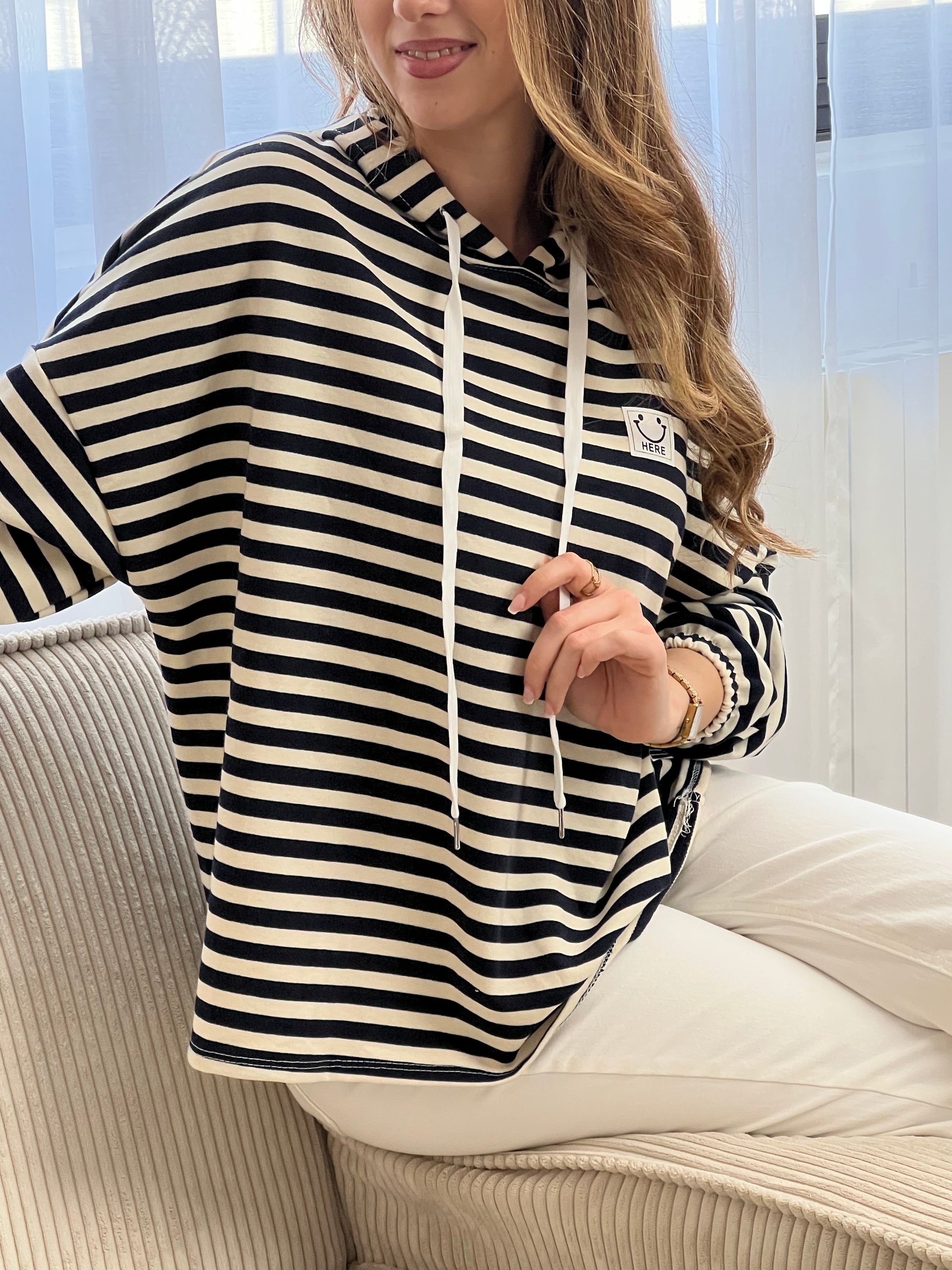 Sweat à capuche en coton à rayures style marinière, idéal pour un look décontracté et tendance. Avec ses manches longues et ses poignets élastiqués, il offre confort et maintien. Sa capuche avec lien de serrage écru et ses rayures horizontales écrues et bleues apportent une touche intemporelle. Agrémenté d’un motif smiley et de l’inscription "Here", ce sweat aux tons bleu marine, beige et écru est parfait pour un style casual moderne.
