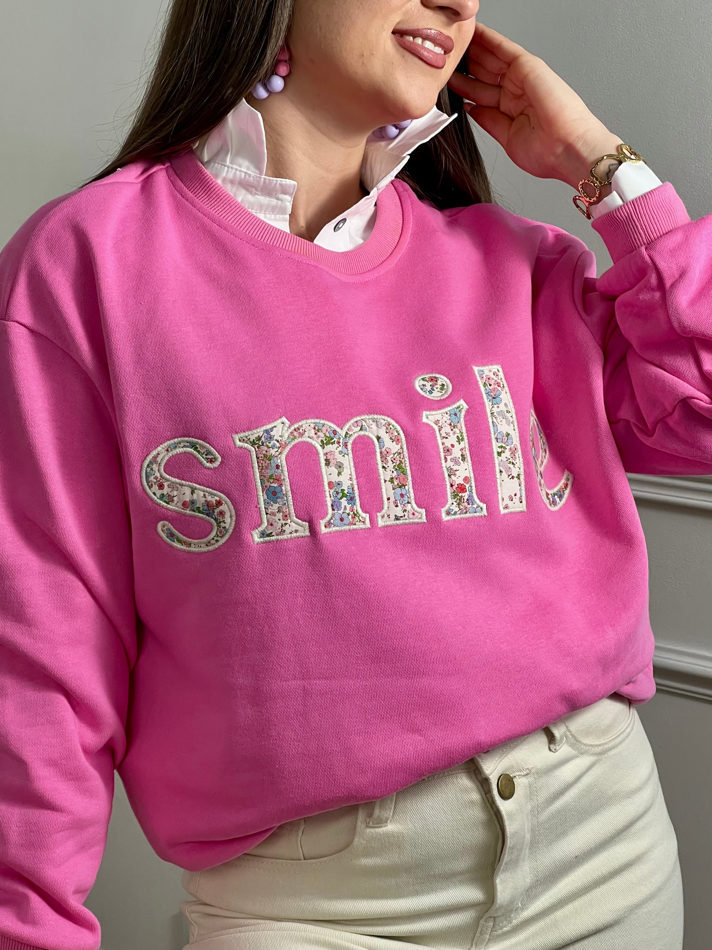 Sweat rose confortable aux manches longues, parfait pour les journées fraîches. Son col rond classique offre une allure intemporelle, tandis que l'inscription "SMILE" brodée avec des motifs fleuris délicats ajoute une touche de personnalité et de douceur. Un basique polyvalent à porter seul ou en superposition, idéal pour exprimer votre style avec bienveillance.