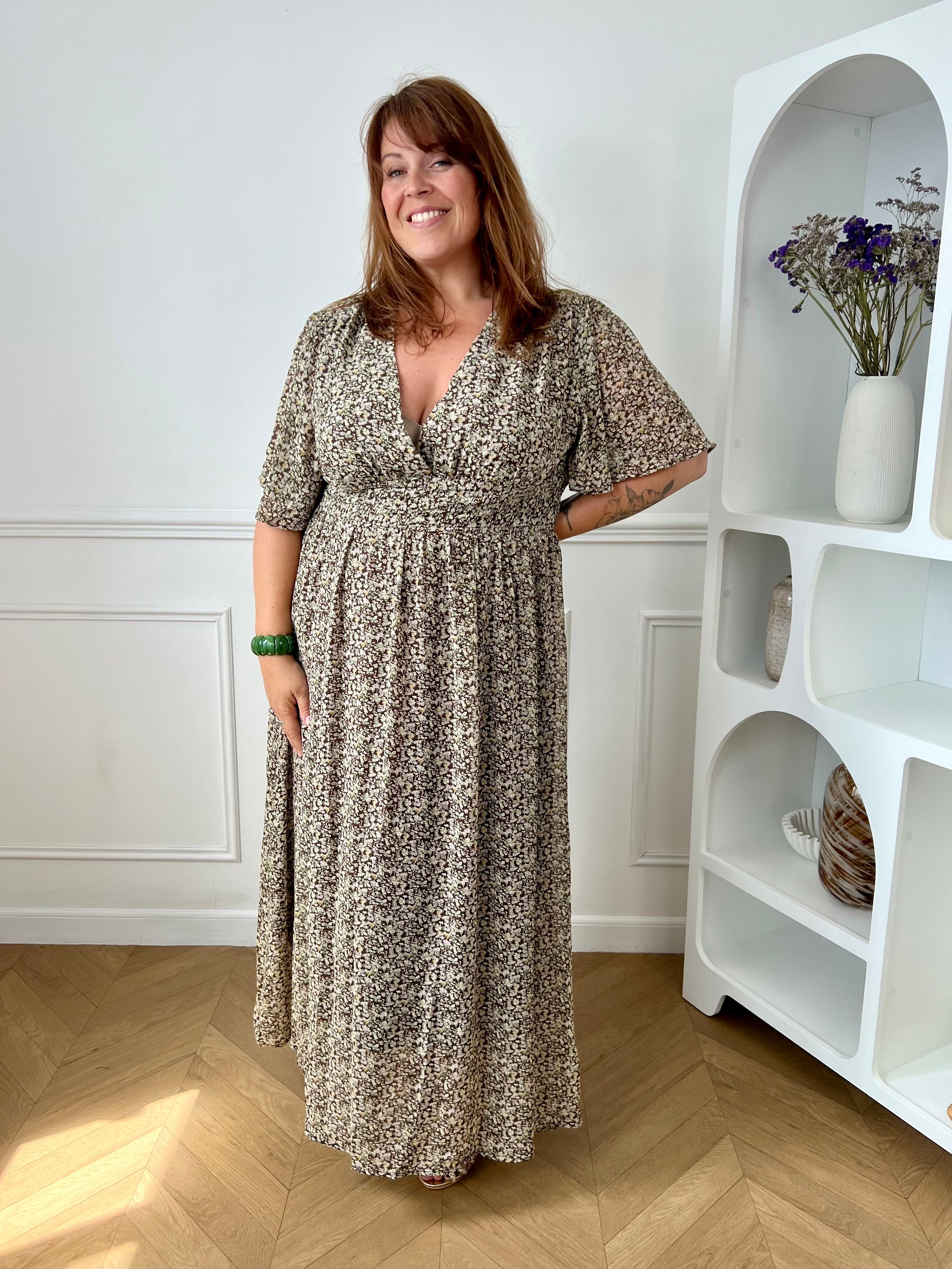 Apportez une touche de couleur et de féminité à votre dressing avec cette robe longue grande taille à motifs fleuris. Son col V et ses manches courtes lui confèrent une allure élégante et légère, tandis que sa taille élastiquée au dos assure un confort optimal et une silhouette harmonieuse. Doublée sur le corps pour plus d’aisance, elle reste légèrement transparente au niveau des manches pour un effet aérien. Ses motifs floraux aux nuances de marron, vert, jaune et rose en font une pièce idéale pour la sais