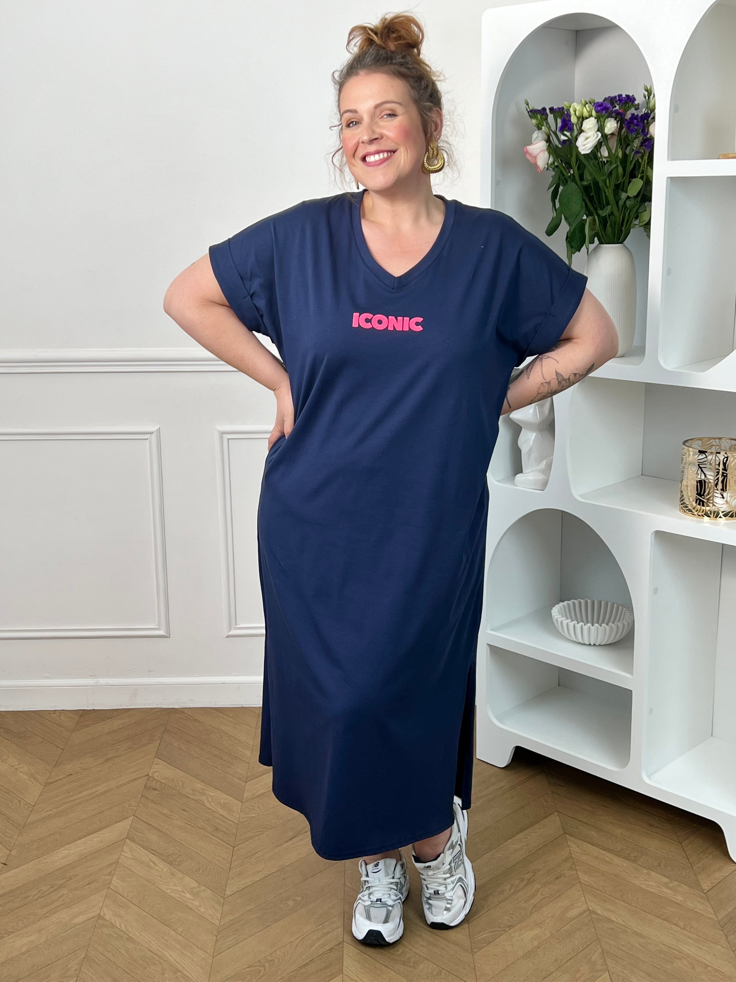 Robe longue bleue grande taille, parfaite pour un look confortable et tendance. Avec sa coupe droite, ses manches courtes et son col V, elle offre une silhouette fluide et agréable à porter. Ses inscriptions à l’avant et au dos apportent une touche moderne et originale. Fendue sur les côtés au bas de la robe, elle assure plus d’aisance et de mouvement. Disponible en bleu marine avec détails rose et orange, cette robe est idéale pour un style décontracté et féminin.