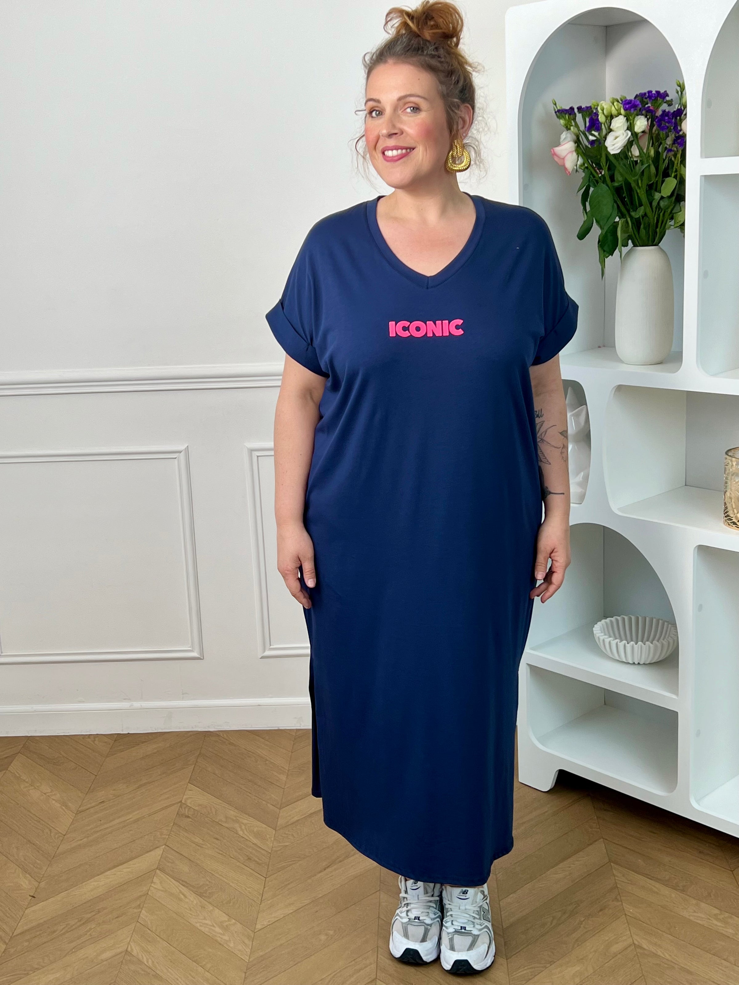 Robe longue bleue grande taille, parfaite pour un look confortable et tendance. Avec sa coupe droite, ses manches courtes et son col V, elle offre une silhouette fluide et agréable à porter. Ses inscriptions à l’avant et au dos apportent une touche moderne et originale. Fendue sur les côtés au bas de la robe, elle assure plus d’aisance et de mouvement. Disponible en bleu marine avec détails rose et orange, cette robe est idéale pour un style décontracté et féminin.