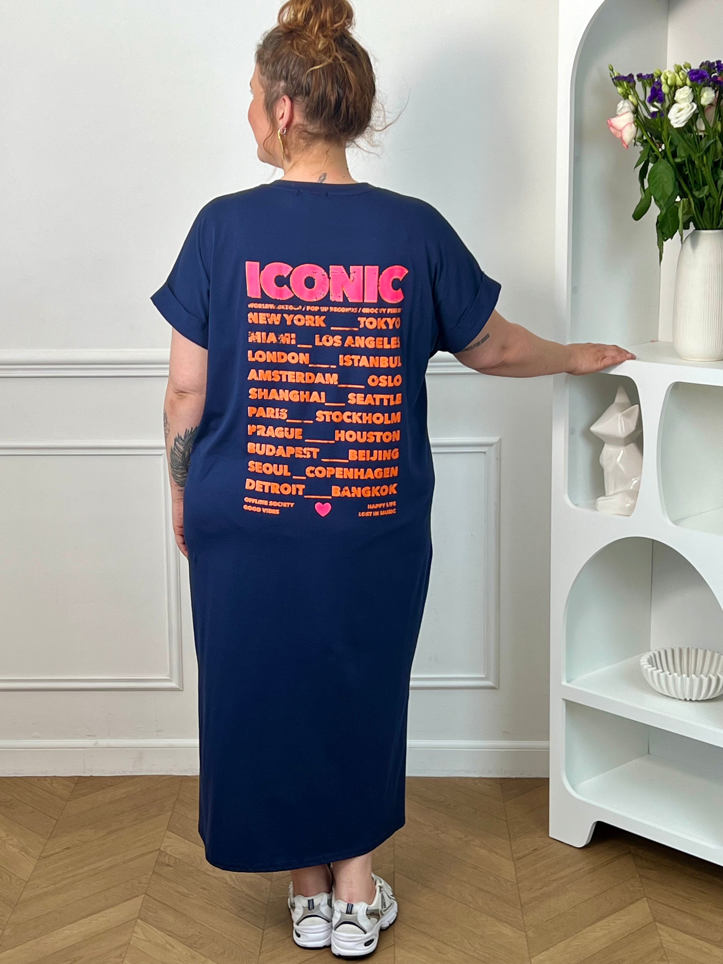 Robe longue bleue grande taille, parfaite pour un look confortable et tendance. Avec sa coupe droite, ses manches courtes et son col V, elle offre une silhouette fluide et agréable à porter. Ses inscriptions à l’avant et au dos apportent une touche moderne et originale. Fendue sur les côtés au bas de la robe, elle assure plus d’aisance et de mouvement. Disponible en bleu marine avec détails rose et orange, cette robe est idéale pour un style décontracté et féminin.