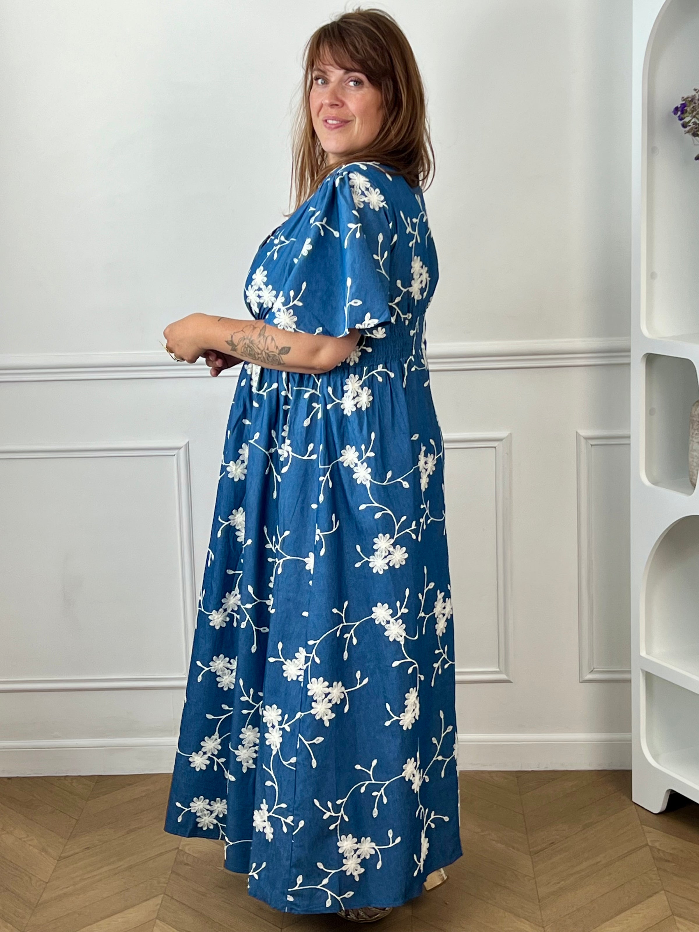 Craquez pour cette robe longue en coton grande taille femme, parfaite pour une allure élégante et confortable. Dotée d'un col V, de manches courtes et d'une taille élastiquée au dos, elle met en valeur la silhouette. Ses délicats motifs fleurs brodés dans des tons bleu marine et écru apportent une touche raffinée, idéale pour la belle saison.