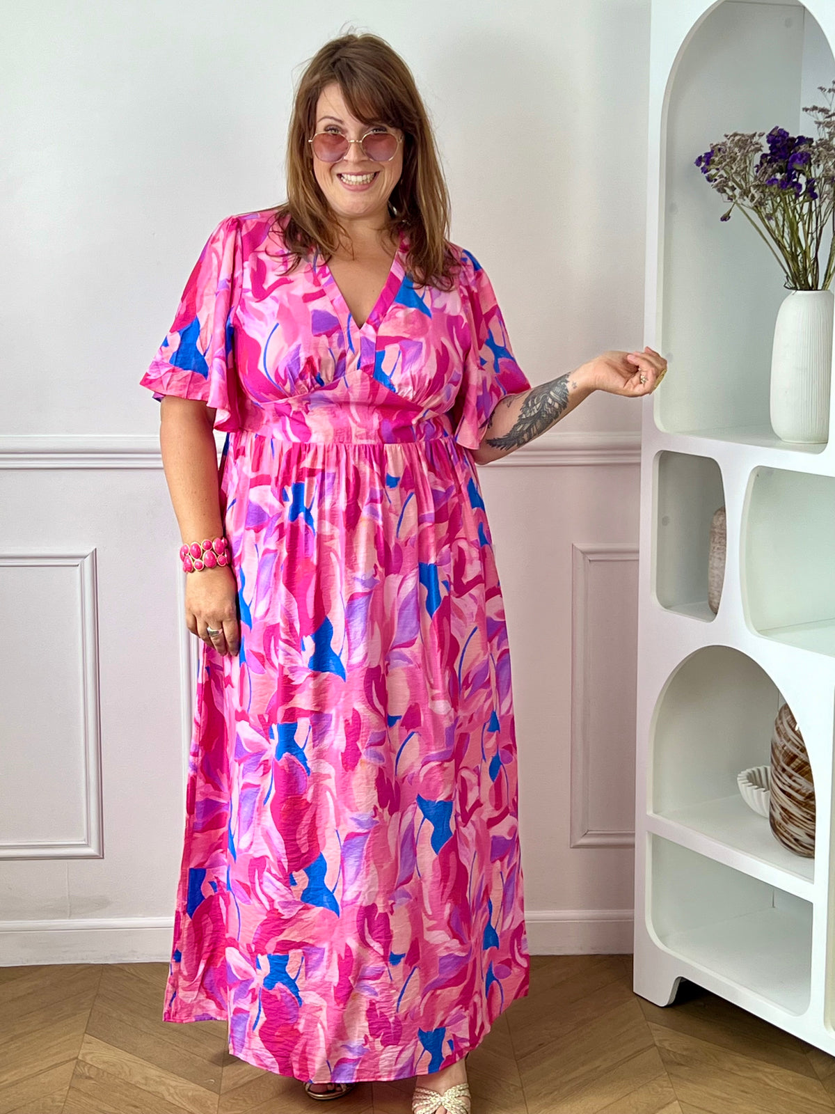 Laissez-vous séduire par cette robe longue grande taille au style féminin et coloré. Son col V et ses manches courtes apportent une touche d’élégance décontractée, tandis que sa taille élastiquée au dos assure un confort optimal et une belle mise en valeur de la silhouette. Sur un fond écru lumineux, ses motifs aux nuances rose fuchsia, jaune, bleu et violet apportent fraîcheur et originalité, faisant de cette robe la pièce idéale pour la saison.