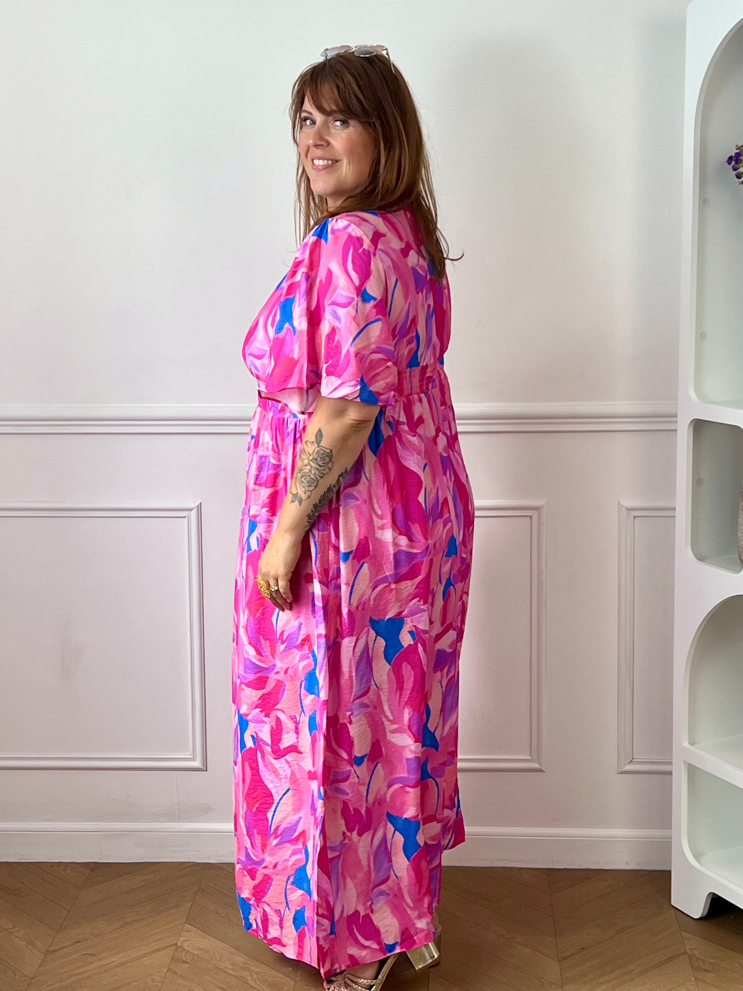Laissez-vous séduire par cette robe longue grande taille au style féminin et coloré. Son col V et ses manches courtes apportent une touche d’élégance décontractée, tandis que sa taille élastiquée au dos assure un confort optimal et une belle mise en valeur de la silhouette. Sur un fond écru lumineux, ses motifs aux nuances rose fuchsia, jaune, bleu et violet apportent fraîcheur et originalité, faisant de cette robe la pièce idéale pour la saison.