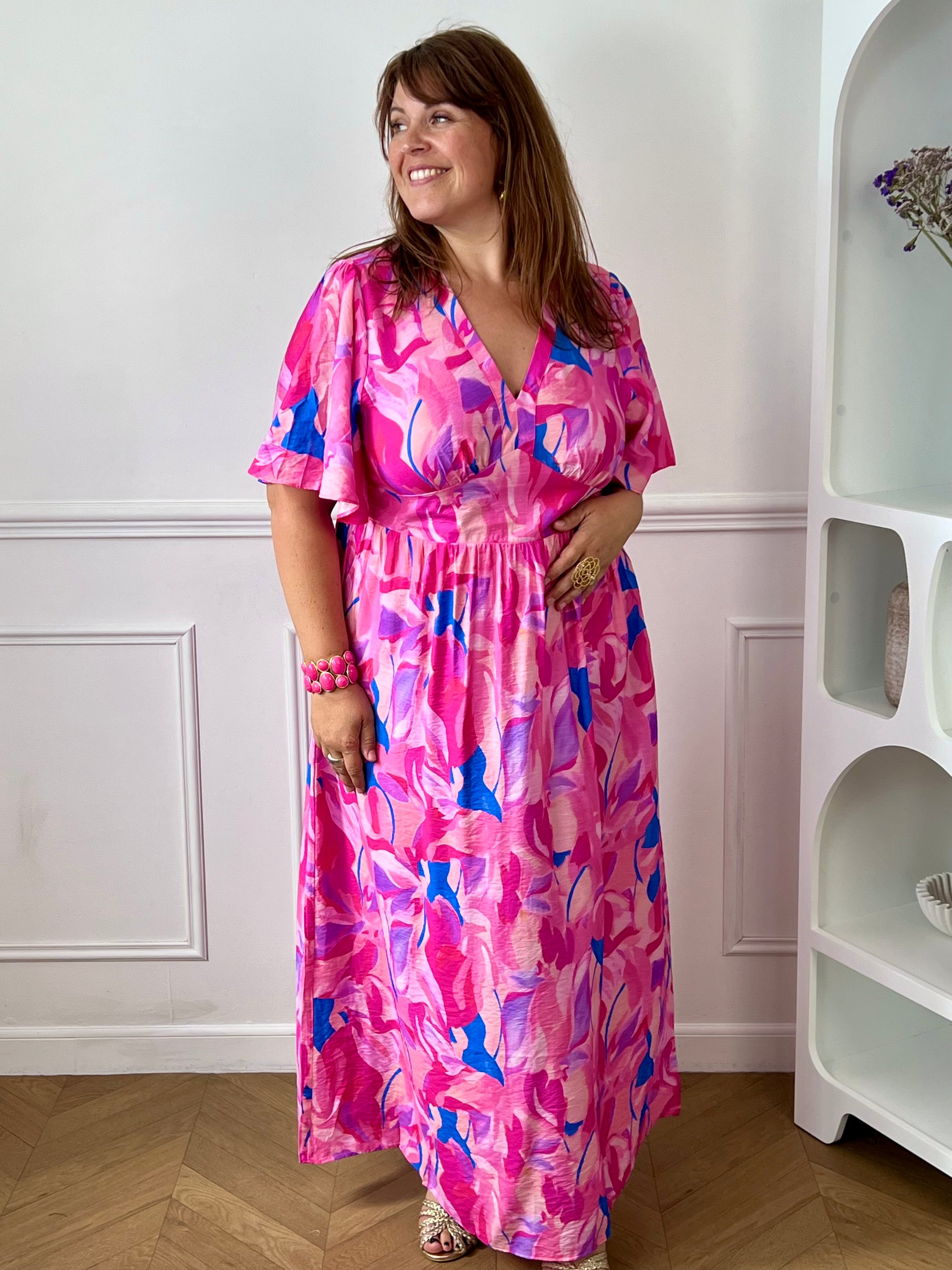 Laissez-vous séduire par cette robe longue grande taille au style féminin et coloré. Son col V et ses manches courtes apportent une touche d’élégance décontractée, tandis que sa taille élastiquée au dos assure un confort optimal et une belle mise en valeur de la silhouette. Sur un fond écru lumineux, ses motifs aux nuances rose fuchsia, jaune, bleu et violet apportent fraîcheur et originalité, faisant de cette robe la pièce idéale pour la saison.