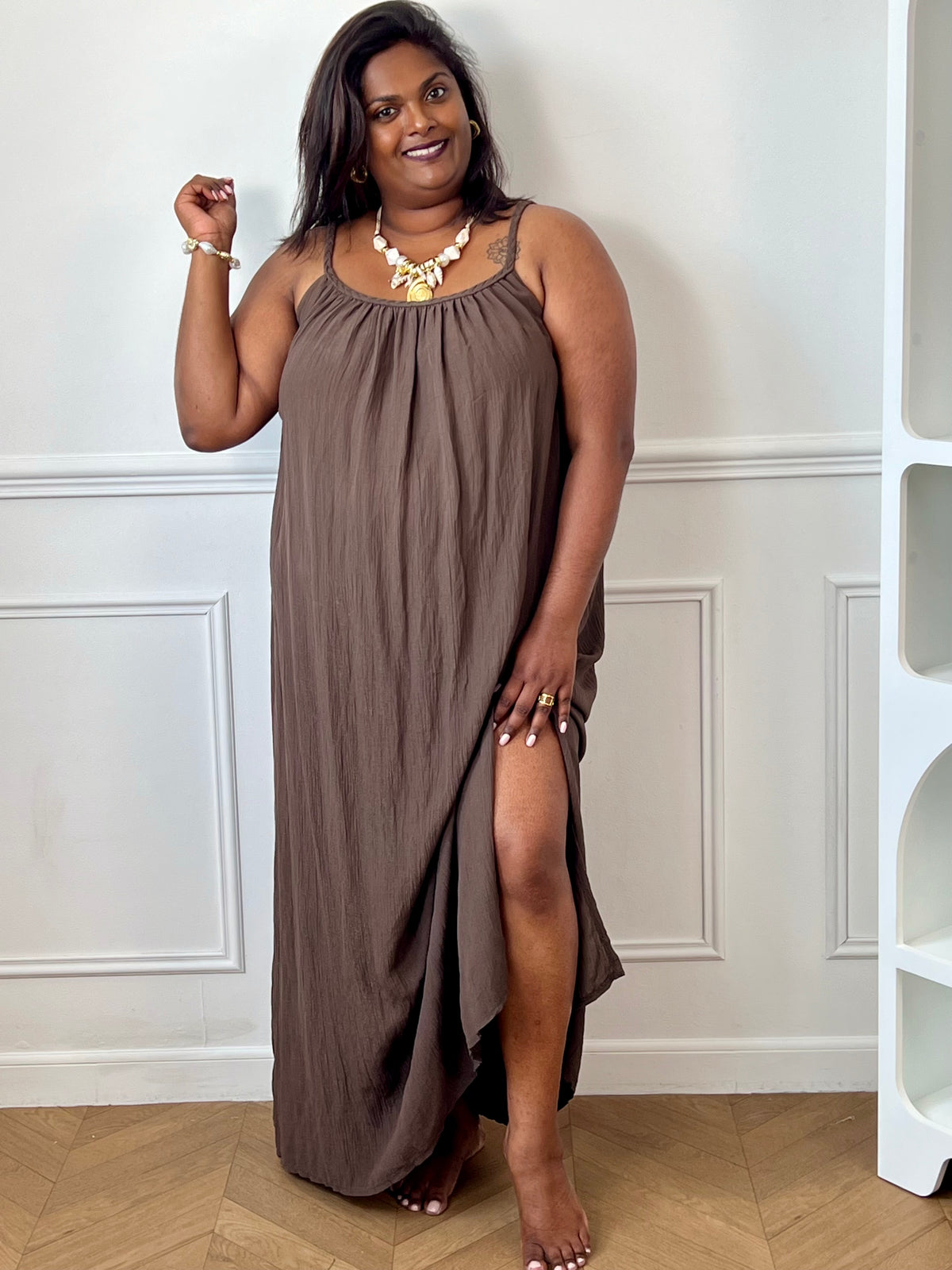 Robe longue marron femme grande taille, à la coupe ample et confortable. Dotée d’un col rond, de bretelles tressées non réglables et d’un élastique au dos pour un meilleur maintien. Ses fentes sur les côtés apportent fluidité et aisance, tandis que le fil lurex doré ajoute une touche lumineuse et élégante. Une robe idéale pour un look chic et décontracté.