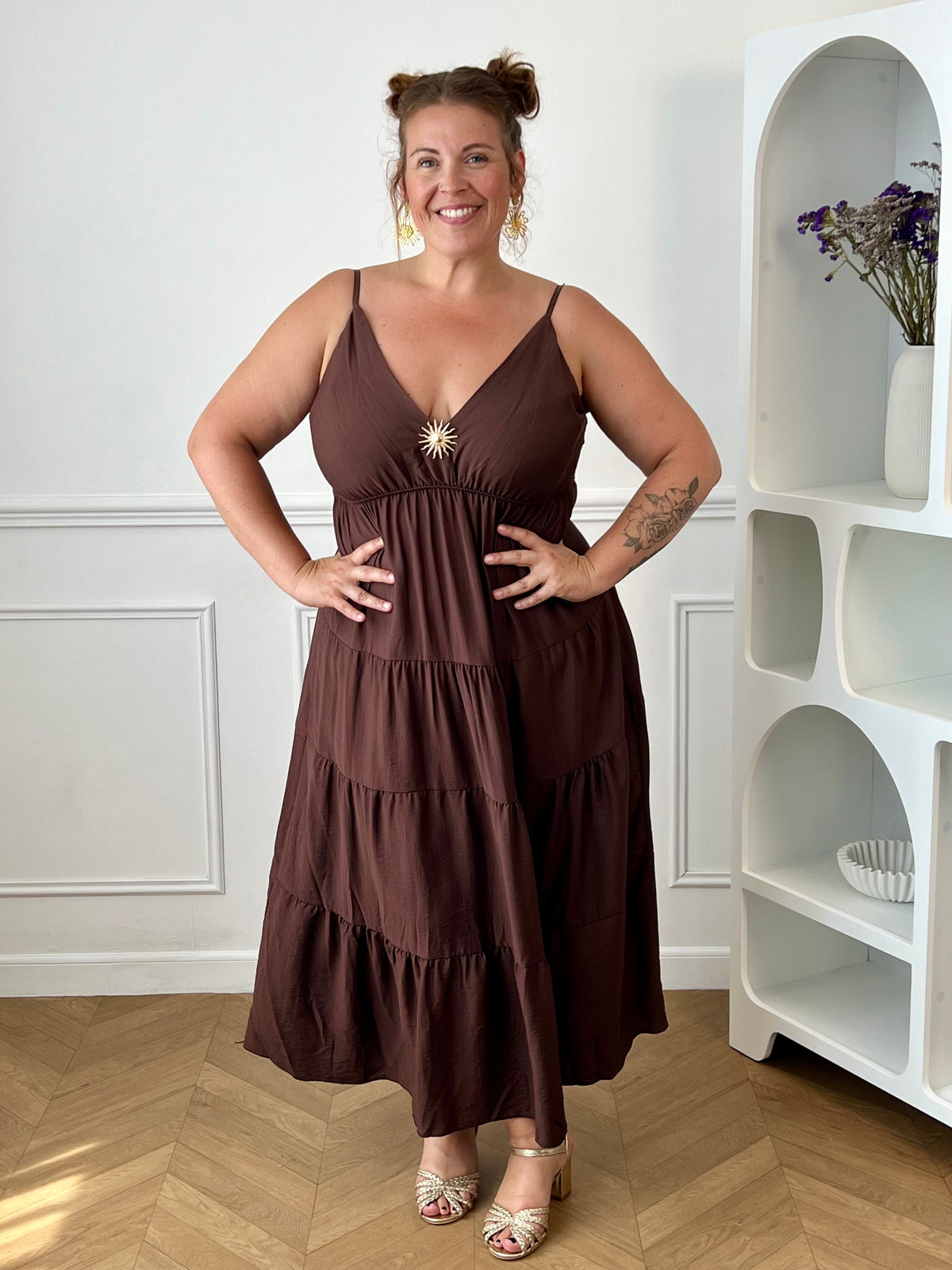 Apportez une touche d'élégance à votre garde-robe avec cette robe longue à bretelles femme. Son col V met délicatement la silhouette en valeur, tandis que les bretelles réglables et l'élastique au dos assurent un ajustement confortable et personnalisé. La broche dorée amovible en forme de soleil apporte une finition raffinée et originale, idéale pour sublimer cette robe marron foncé. Une pièce chic et intemporelle, parfaite pour vos journées d'été comme pour vos occasions spéciales.