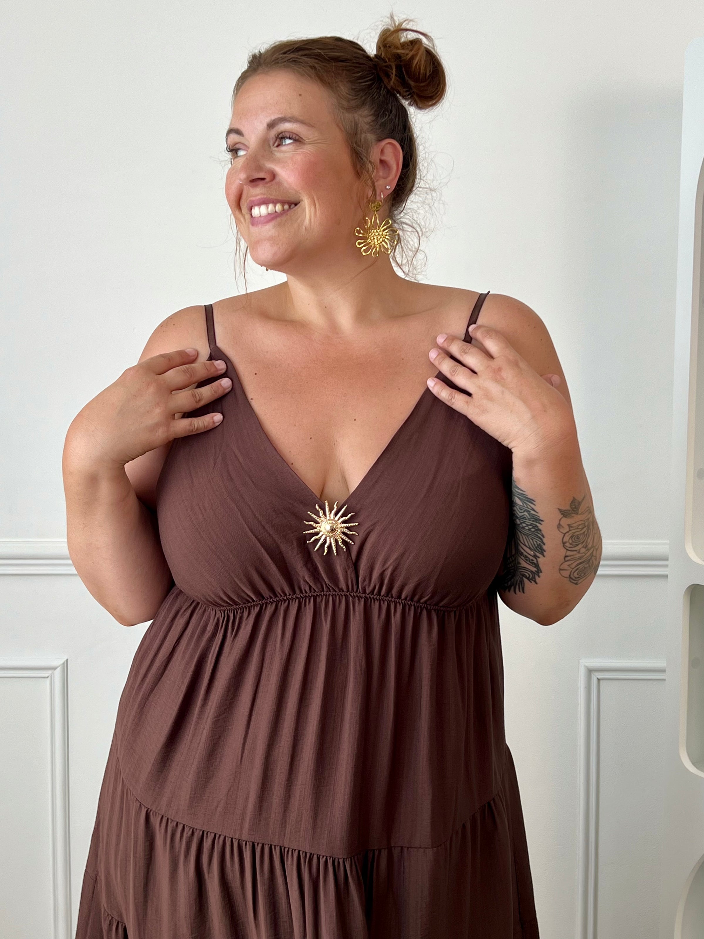 Apportez une touche d'élégance à votre garde-robe avec cette robe longue à bretelles femme. Son col V met délicatement la silhouette en valeur, tandis que les bretelles réglables et l'élastique au dos assurent un ajustement confortable et personnalisé. La broche dorée amovible en forme de soleil apporte une finition raffinée et originale, idéale pour sublimer cette robe marron foncé. Une pièce chic et intemporelle, parfaite pour vos journées d'été comme pour vos occasions spéciales.