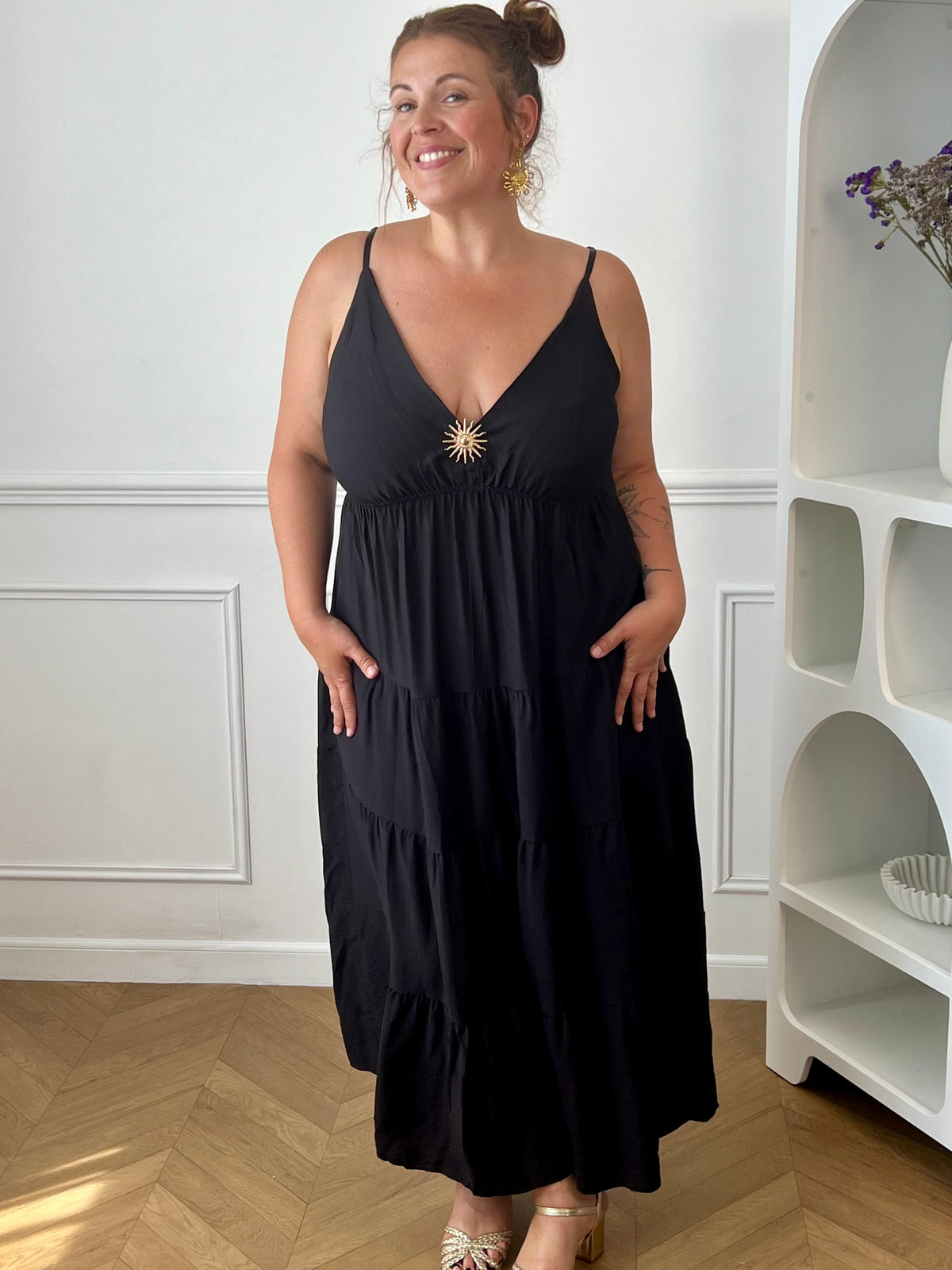 Apportez une touche d'élégance à votre garde-robe avec cette robe longue à bretelles femme. Son col V met délicatement la silhouette en valeur, tandis que les bretelles réglables et l'élastique au dos assurent un ajustement confortable et personnalisé. La broche dorée amovible en forme de soleil apporte une finition raffinée et originale, idéale pour sublimer cette robe noire. Une pièce chic et intemporelle, parfaite pour vos journées d'été comme pour vos occasions spéciales.