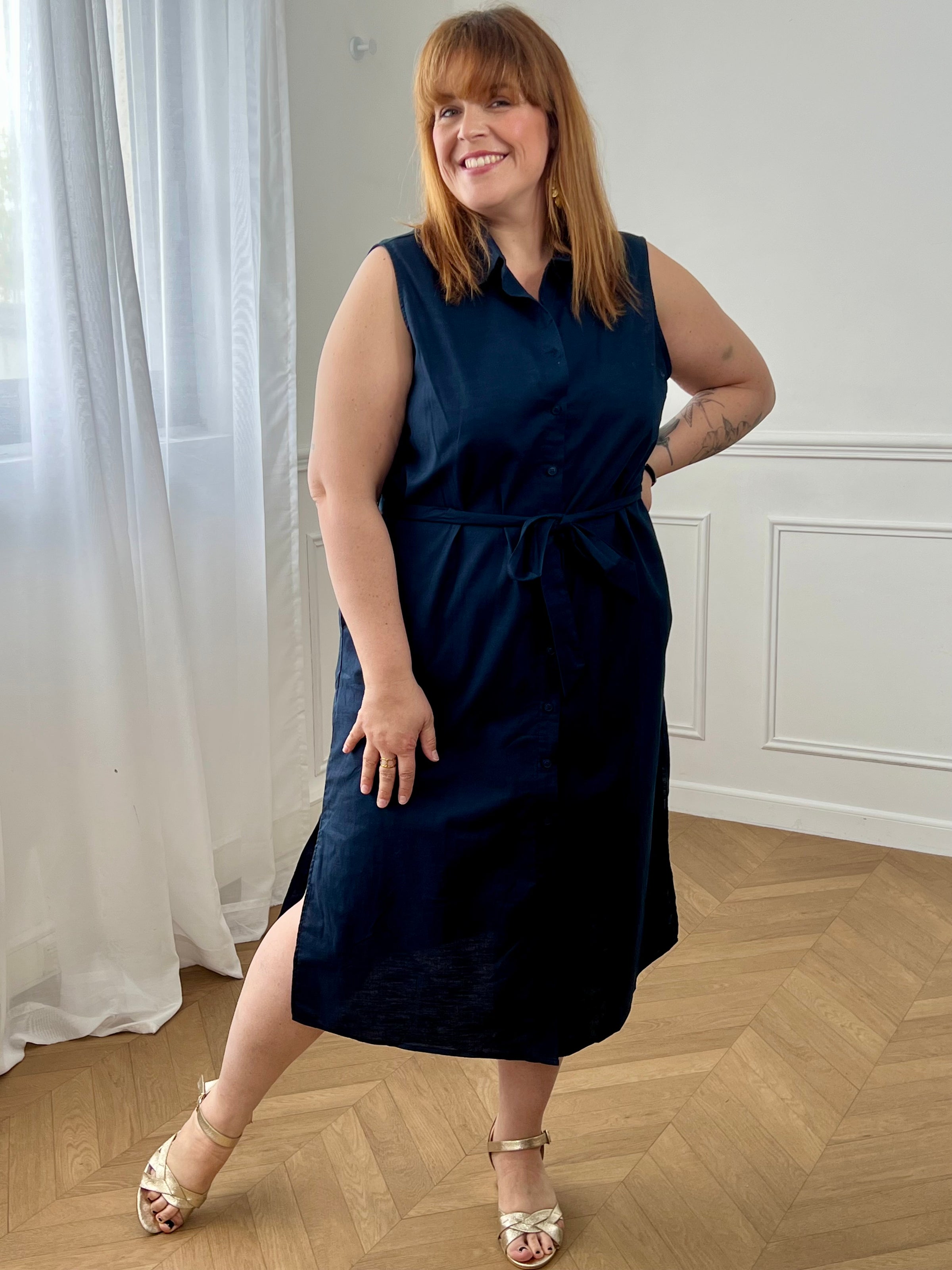 Adoptez cette robe en coton grande taille, à la fois confortable et structurée. Dotée d’un col chemise et de manches courtes avec revers, elle se ferme par des boutons. Sa ceinture amovible avec passants permet de marquer la taille. En noir, c’est une pièce intemporelle facile à porter au quotidien.
