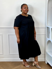 Robe midi noire grande taille avec poches latérales, portée avec des sandales pour un look élégant.