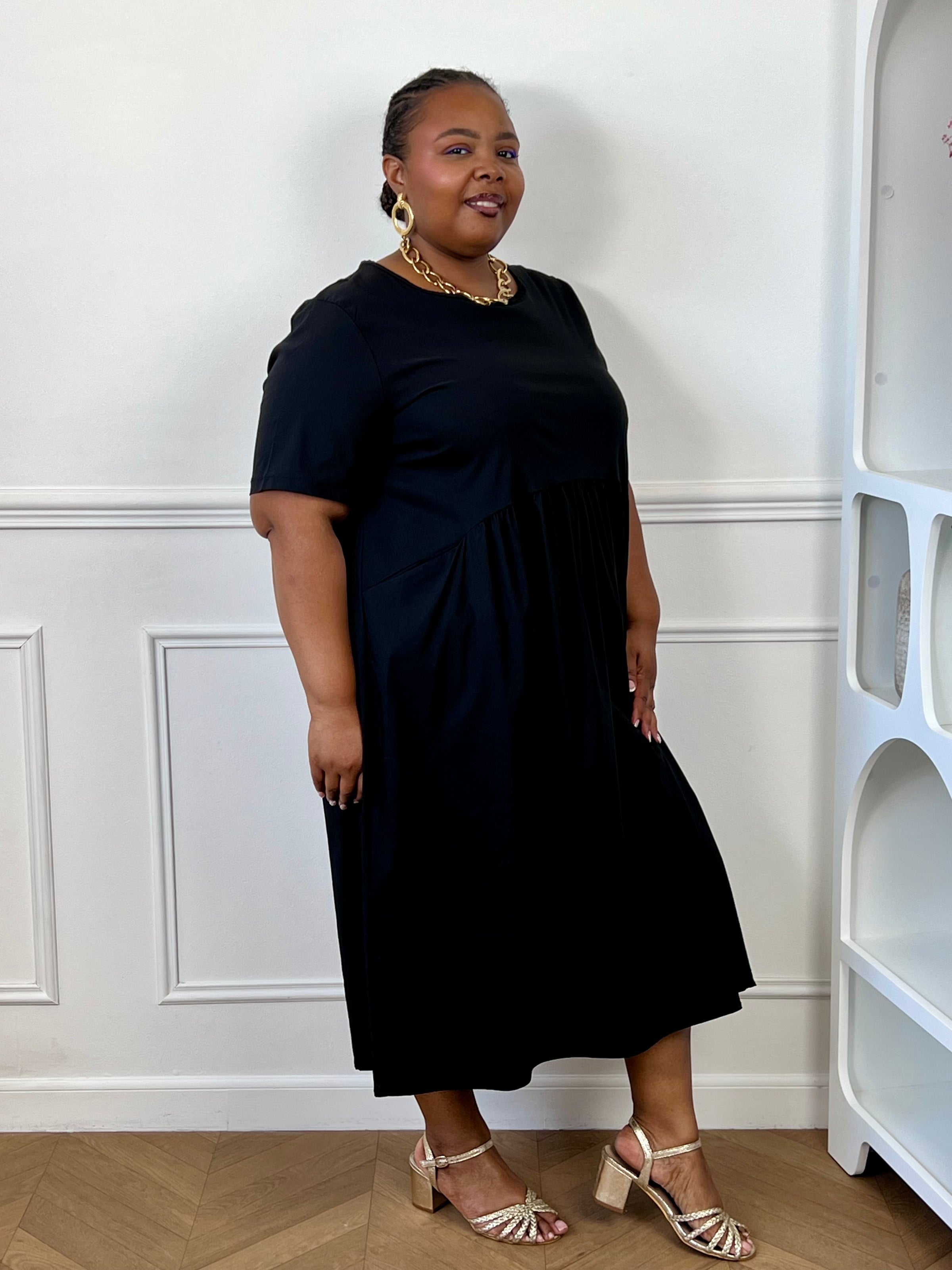 Robe midi noire grande taille avec poches latérales, portée avec des sandales pour un look élégant.