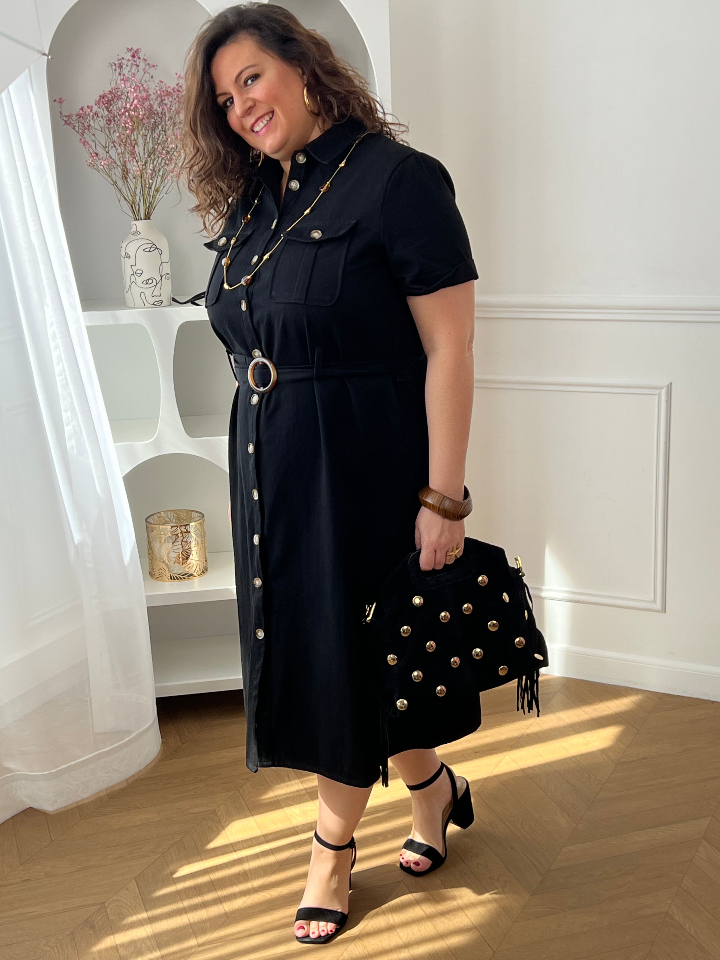 Adoptez cette robe en coton grande taille, à la fois confortable et structurée. Dotée d’un col chemise et de manches courtes avec revers, elle se ferme par des boutons. Sa ceinture amovible avec passants permet de marquer la taille. En noir, c’est une pièce intemporelle facile à porter au quotidien.