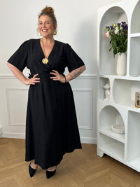Sublimez votre silhouette avec cette robe longue grande taille au style élégant et féminin. Son col cache-cœur met délicatement le décolleté en valeur, tandis que l’élastique à la taille et aux poignets assure un confort optimal et un ajustement parfait. Le lien à nouer à la taille crée un joli effet portefeuille qui souligne la silhouette avec raffinement. Avec ses manches courtes et sa couleur noire intemporelle, cette robe est idéale pour toutes les occasions, du quotidien aux événements plus habillés.