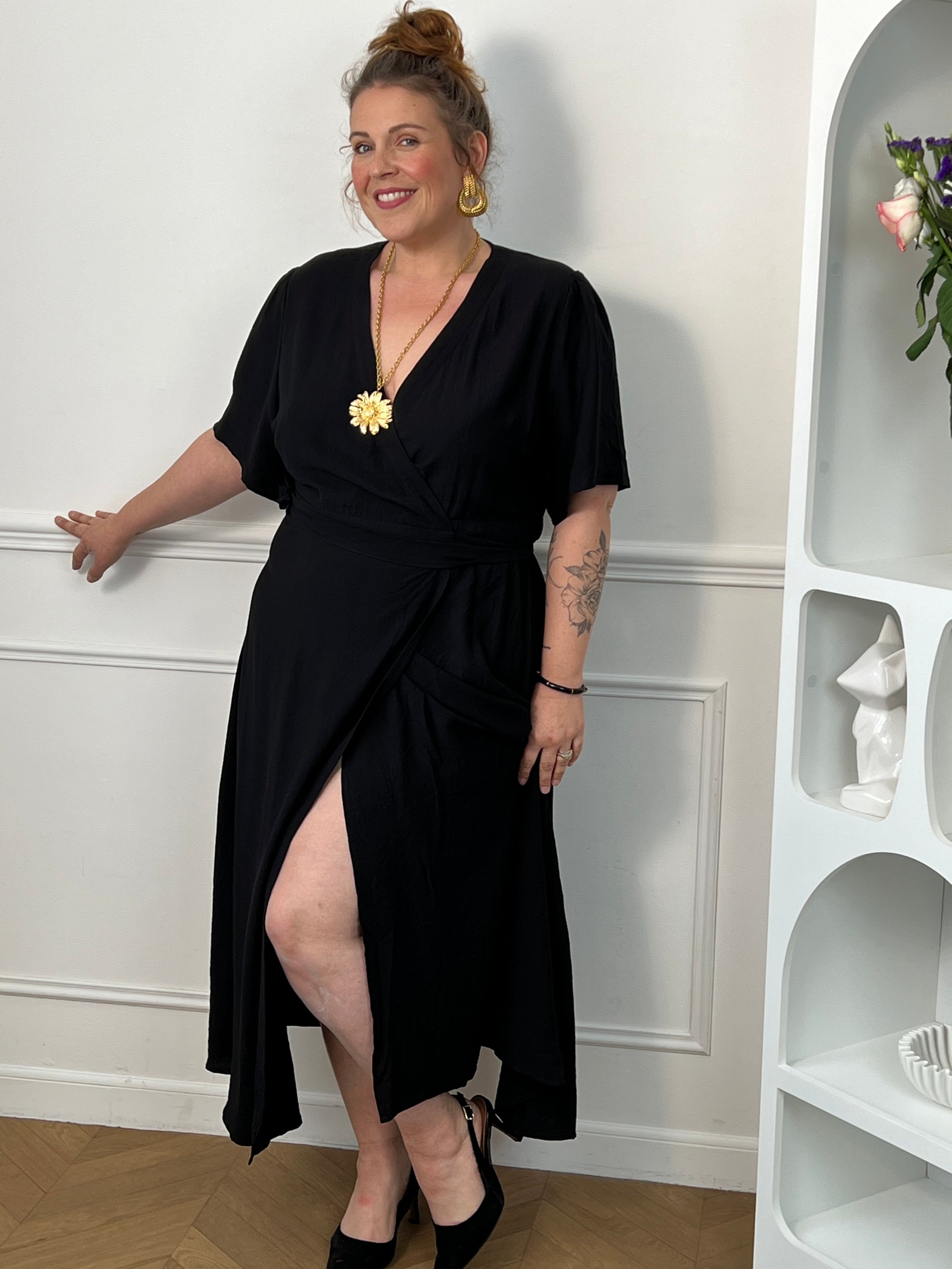 Sublimez votre silhouette avec cette robe longue grande taille au style élégant et féminin. Son col cache-cœur met délicatement le décolleté en valeur, tandis que l’élastique à la taille et aux poignets assure un confort optimal et un ajustement parfait. Le lien à nouer à la taille crée un joli effet portefeuille qui souligne la silhouette avec raffinement. Avec ses manches courtes et sa couleur noire intemporelle, cette robe est idéale pour toutes les occasions, du quotidien aux événements plus habillés.