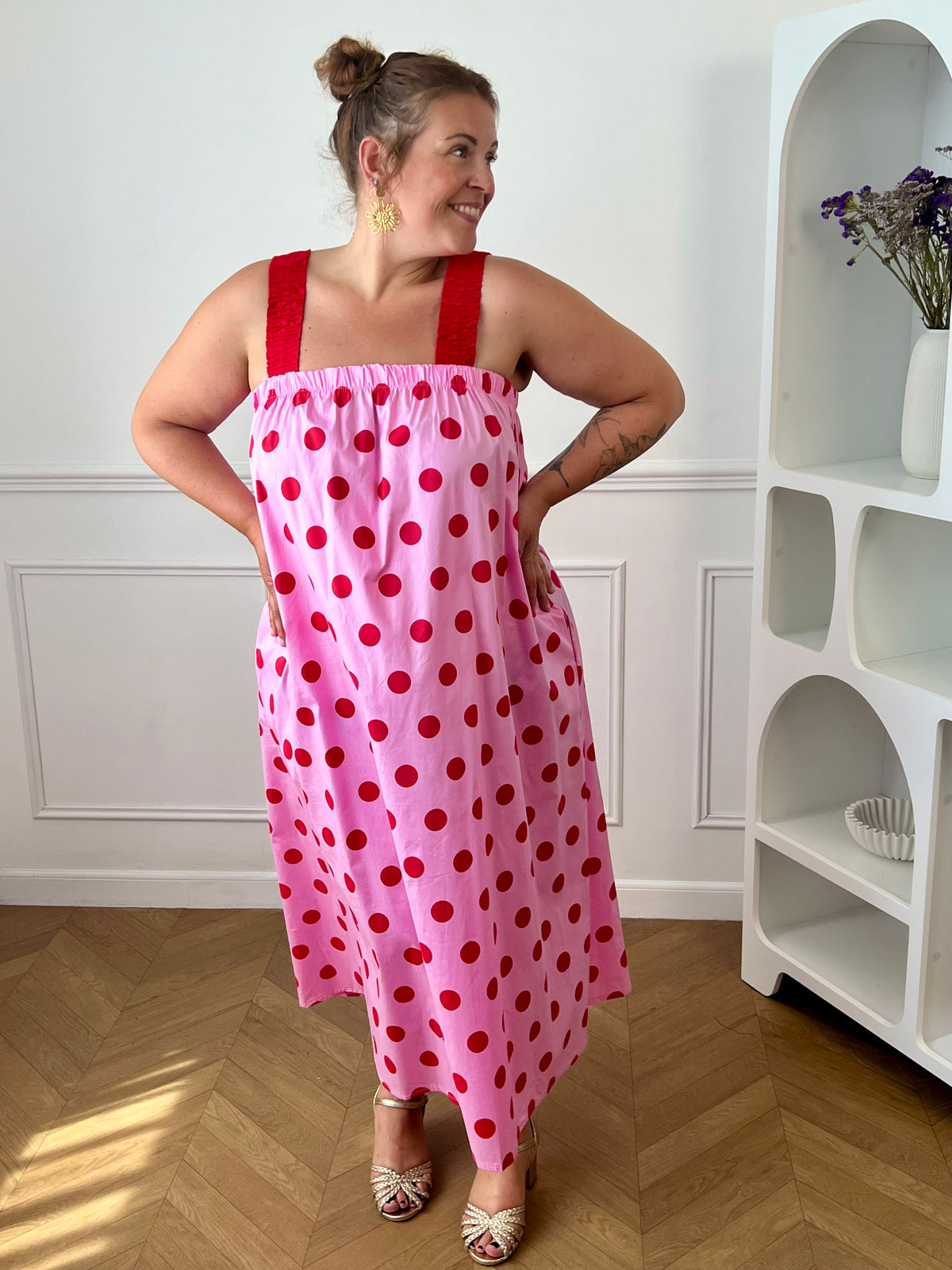 Craquez pour cette robe longue grande taille au style doux et féminin. Son col carré élastiqué et ses bretelles élastiques assurent un confort optimal tout au long de la journée. Pratique grâce à ses deux poches latérales, elle séduit également par sa coupe droite qui offre une silhouette fluide et agréable à porter. Ses motifs pois rouges sur fond rose apportent une touche romantique et tendance, tandis que sa confection en 100% coton garantit légèreté et confort au quotidien.