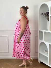 Craquez pour cette robe longue grande taille au style doux et féminin. Son col carré élastiqué et ses bretelles élastiques assurent un confort optimal tout au long de la journée. Pratique grâce à ses deux poches latérales, elle séduit également par sa coupe droite qui offre une silhouette fluide et agréable à porter. Ses motifs pois rouges sur fond rose apportent une touche romantique et tendance, tandis que sa confection en 100% coton garantit légèreté et confort au quotidien.