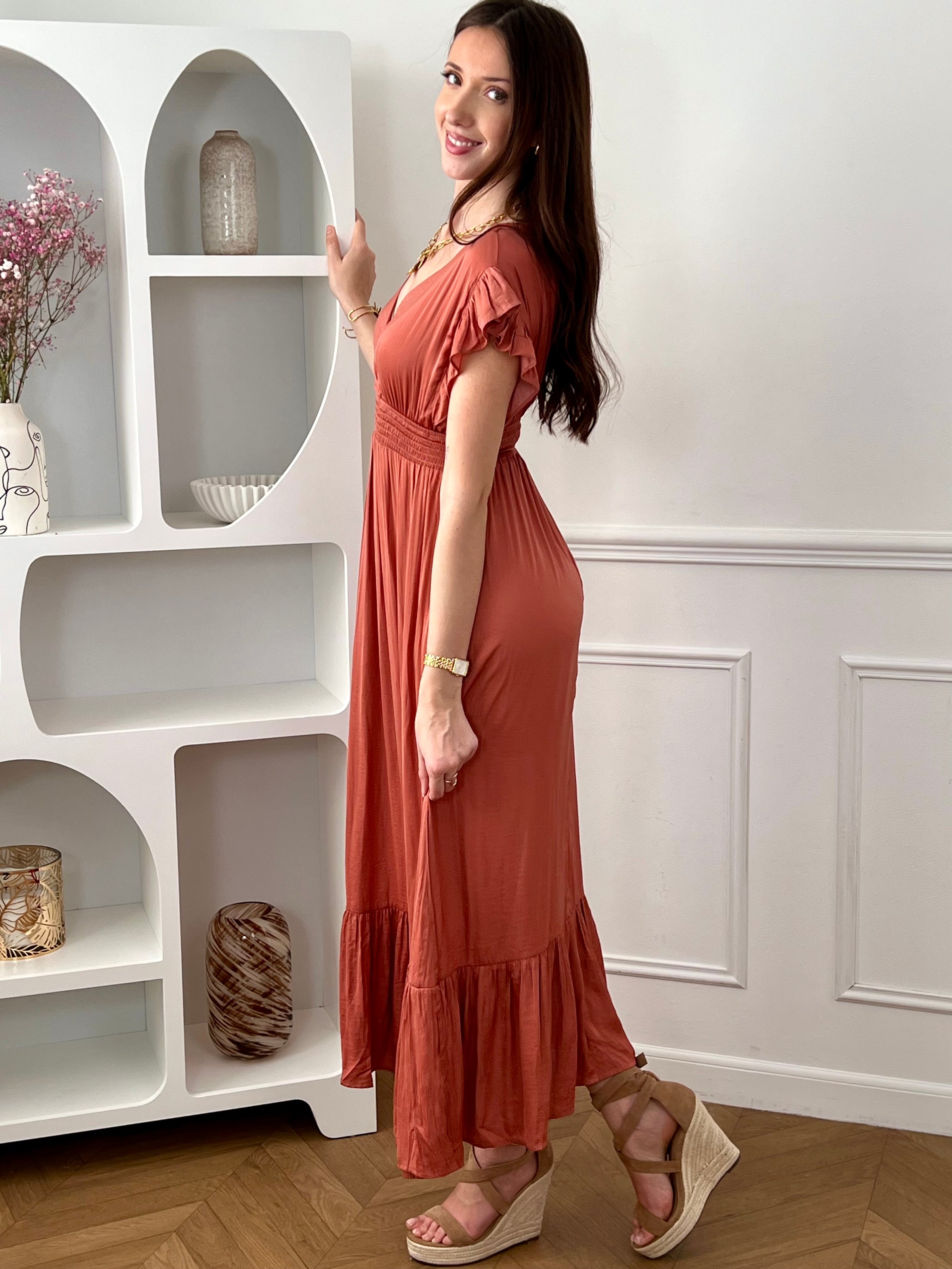 Craquez pour cette robe longue femme terracotta, élégante et féminine. Sans manches, elle se distingue par ses volants aux épaules et son col V plongeant qui sublime le décolleté. Son dos nu avec lien à nouer apporte une touche raffinée, tandis que sa taille élastique assure confort et maintien. Une pièce idéale pour un look chic et estival.
