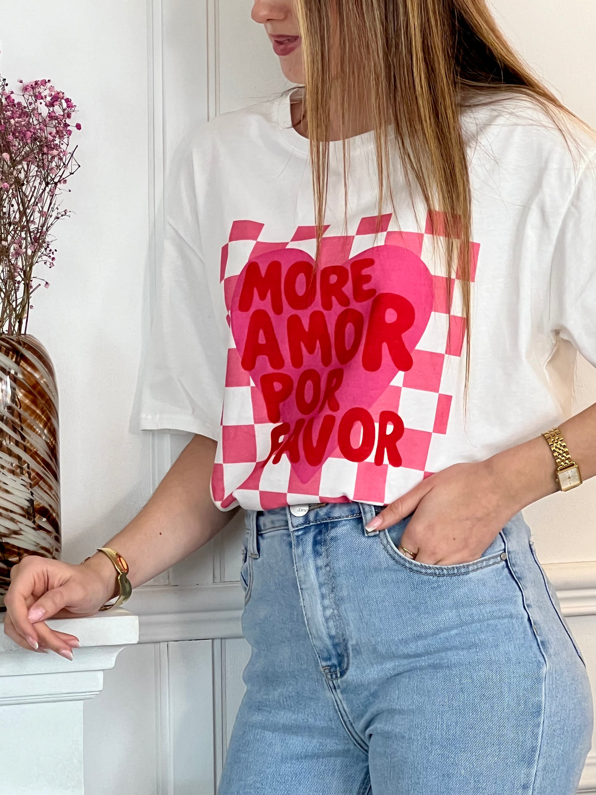 Tee-shirt blanc femme à manches courtes, idéal pour un look tendance et féminin. Doté d’un col V et d’une inscription rose "More Amor Por Favor", il apporte une touche moderne et romantique. Ses motifs cœur et quadrillage ajoutent du style et de l’originalité. Facile à porter au quotidien, ce tee-shirt aux couleurs blanc, rose et rouge est parfait pour une tenue casual chic.