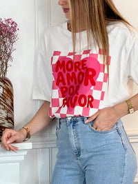 Tee-shirt blanc femme à manches courtes, idéal pour un look tendance et féminin. Doté d’un col V et d’une inscription rose "More Amor Por Favor", il apporte une touche moderne et romantique. Ses motifs cœur et quadrillage ajoutent du style et de l’originalité. Facile à porter au quotidien, ce tee-shirt aux couleurs blanc, rose et rouge est parfait pour une tenue casual chic.