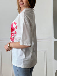 Tee-shirt blanc femme à manches courtes, idéal pour un look tendance et féminin. Doté d’un col V et d’une inscription rose "More Amor Por Favor", il apporte une touche moderne et romantique. Ses motifs cœur et quadrillage ajoutent du style et de l’originalité. Facile à porter au quotidien, ce tee-shirt aux couleurs blanc, rose et rouge est parfait pour une tenue casual chic.