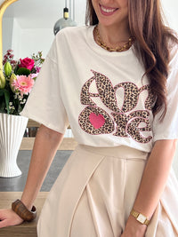 Tee-shirt blanc femme avec inscription "Amore" en motif léopard, parfait pour un look tendance et féminin. Conçu en 100% coton, il offre un confort optimal au quotidien grâce à ses manches courtes et son col rond. Ses touches de couleurs rose, beige, noir et marron apportent une note originale et facile à assortir. Un basique revisité, idéal pour un style chic et décontracté.