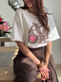 Tee-shirt blanc femme avec inscription "Amore" en motif léopard, parfait pour un look tendance et féminin. Conçu en 100% coton, il offre un confort optimal au quotidien grâce à ses manches courtes et son col rond. Ses touches de couleurs rose, beige, noir et marron apportent une note originale et facile à assortir. Un basique revisité, idéal pour un style chic et décontracté.