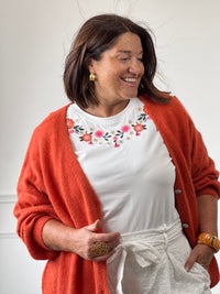 Tee-shirt blanc fleuri porté avec un gilet orange pour un look coloré et tendance.