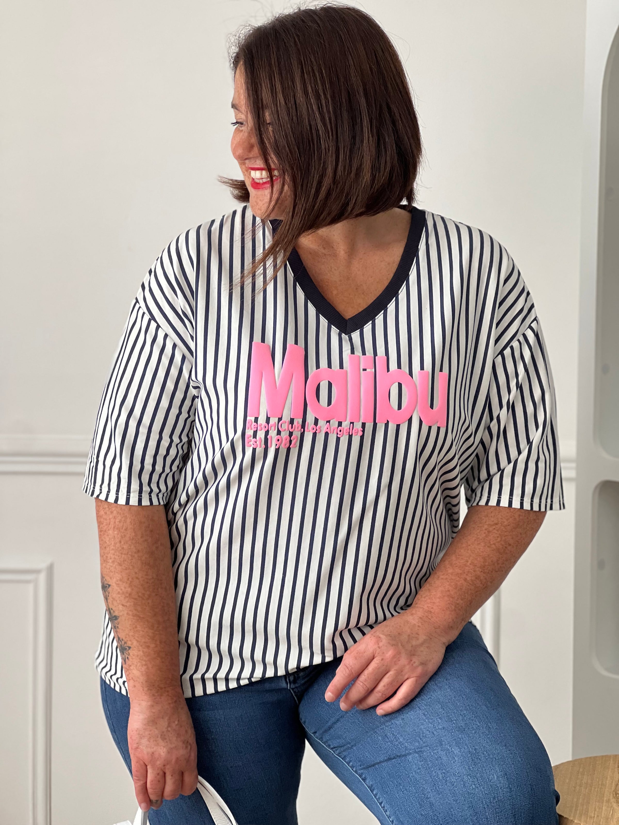 Apportez une touche de fraîcheur à vos tenues avec ce tee-shirt femme aux accents colorés et estivaux. Confectionné en 100% coton, il offre un confort optimal grâce à sa matière douce et légère. Son col V et ses manches courtes assurent une coupe féminine et agréable à porter, tandis que l’inscription rose « Malibu » apporte une note tendance et décontractée. Les rayures verticales bleu marine et écrues allongent visuellement la silhouette et complètent harmonieusement ce modèle aux teintes bleu marine et r