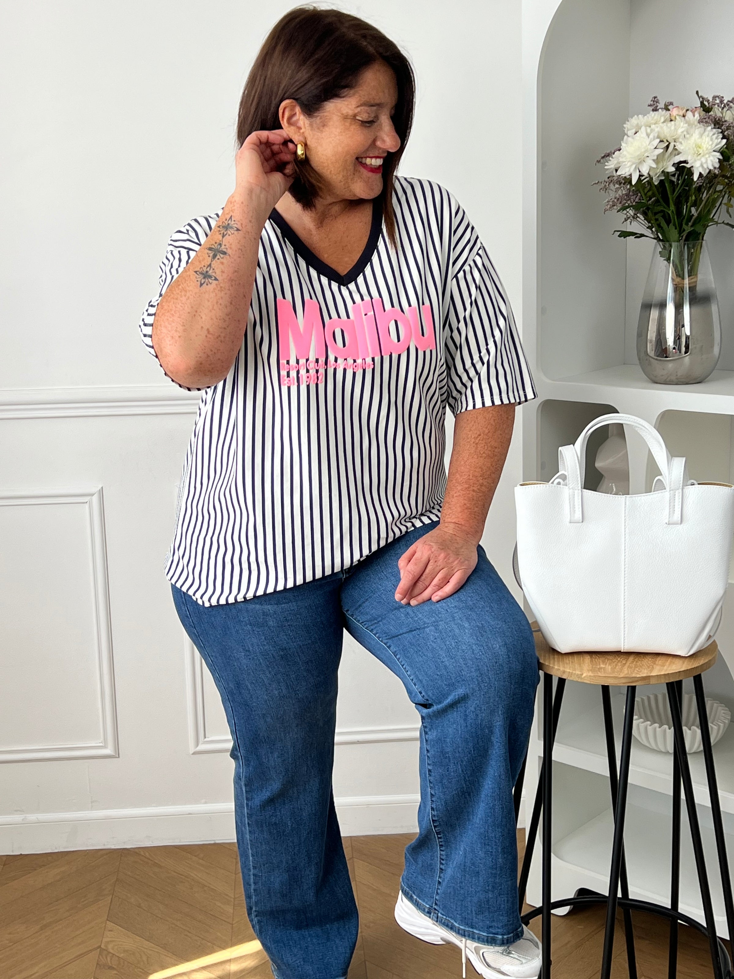 Apportez une touche de fraîcheur à vos tenues avec ce tee-shirt femme aux accents colorés et estivaux. Confectionné en 100% coton, il offre un confort optimal grâce à sa matière douce et légère. Son col V et ses manches courtes assurent une coupe féminine et agréable à porter, tandis que l’inscription rose « Malibu » apporte une note tendance et décontractée. Les rayures verticales bleu marine et écrues allongent visuellement la silhouette et complètent harmonieusement ce modèle aux teintes bleu marine et r