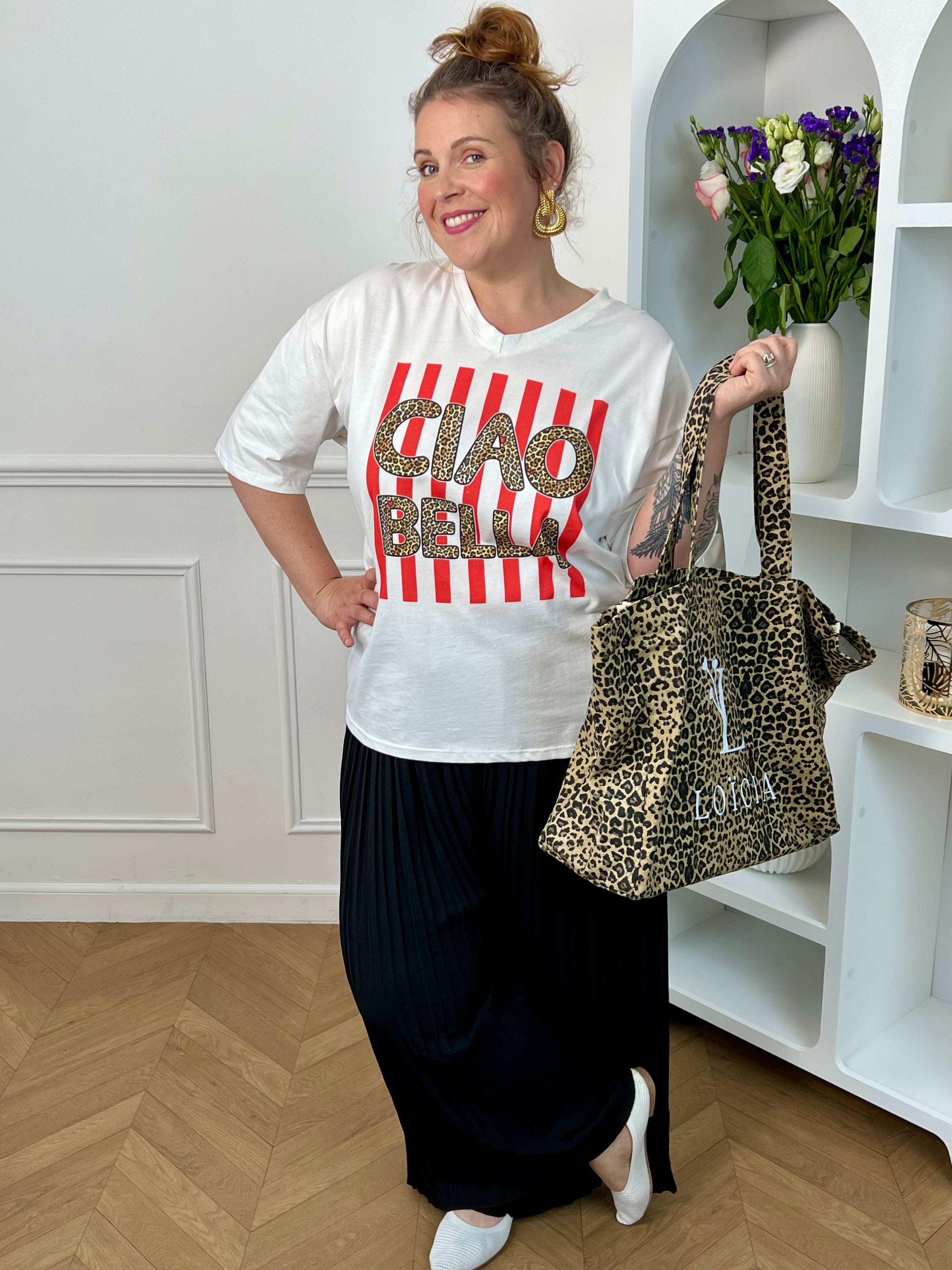 Tee-shirt blanc femme en 100% coton, parfait pour un look tendance et décontracté. Avec ses manches courtes, son col V et son inscription léopard "Ciao Bella", il apporte une touche moderne et originale. Ses rayures rouges verticales ajoutent du style et du caractère à la tenue. Confortable et facile à associer, ce tee-shirt aux tons blanc, rose, beige, noir et marron est idéal pour un look casual chic au quotidien.
