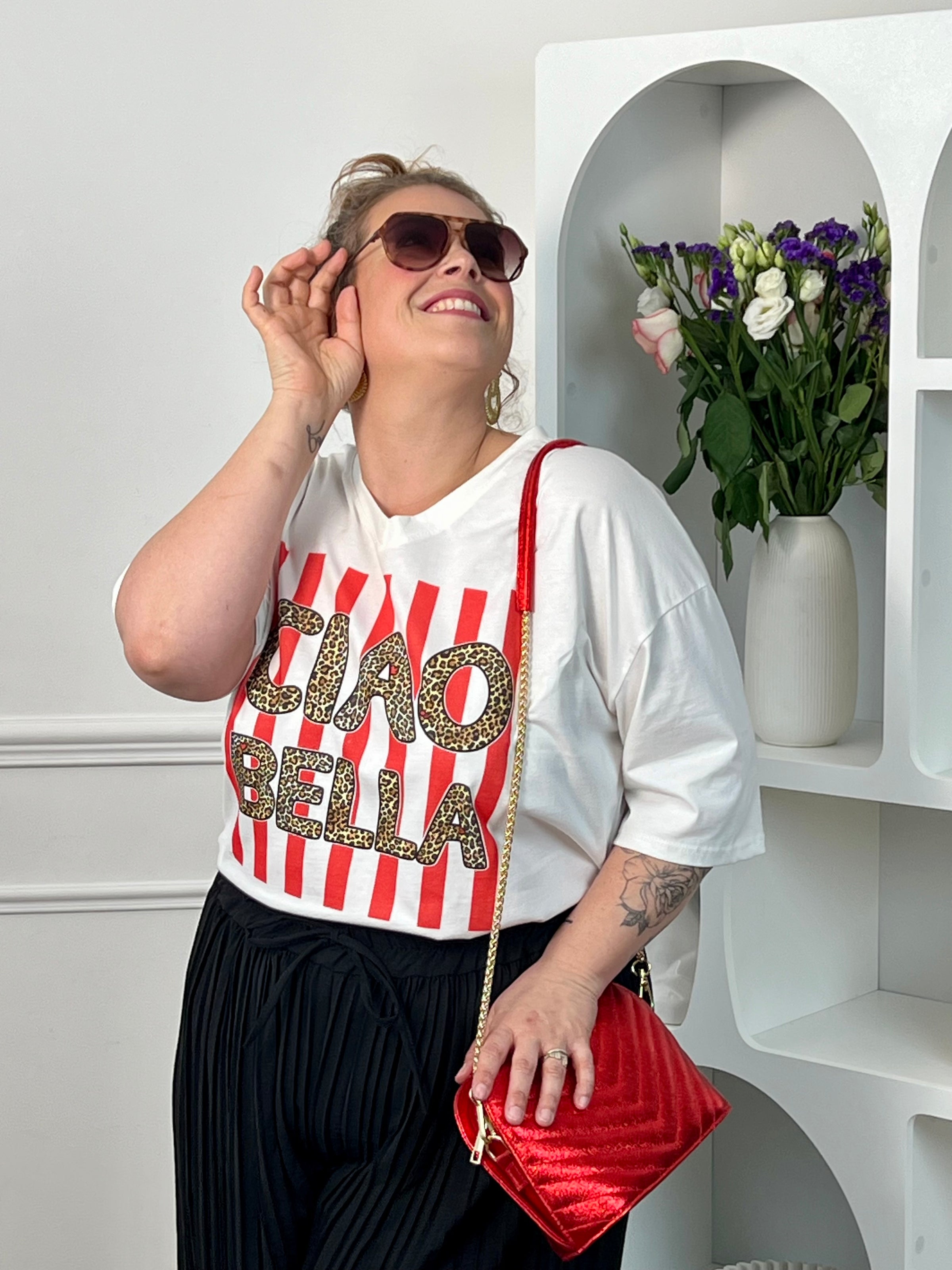 Tee-shirt blanc femme en 100% coton, parfait pour un look tendance et décontracté. Avec ses manches courtes, son col V et son inscription léopard "Ciao Bella", il apporte une touche moderne et originale. Ses rayures rouges verticales ajoutent du style et du caractère à la tenue. Confortable et facile à associer, ce tee-shirt aux tons blanc, rose, beige, noir et marron est idéal pour un look casual chic au quotidien.