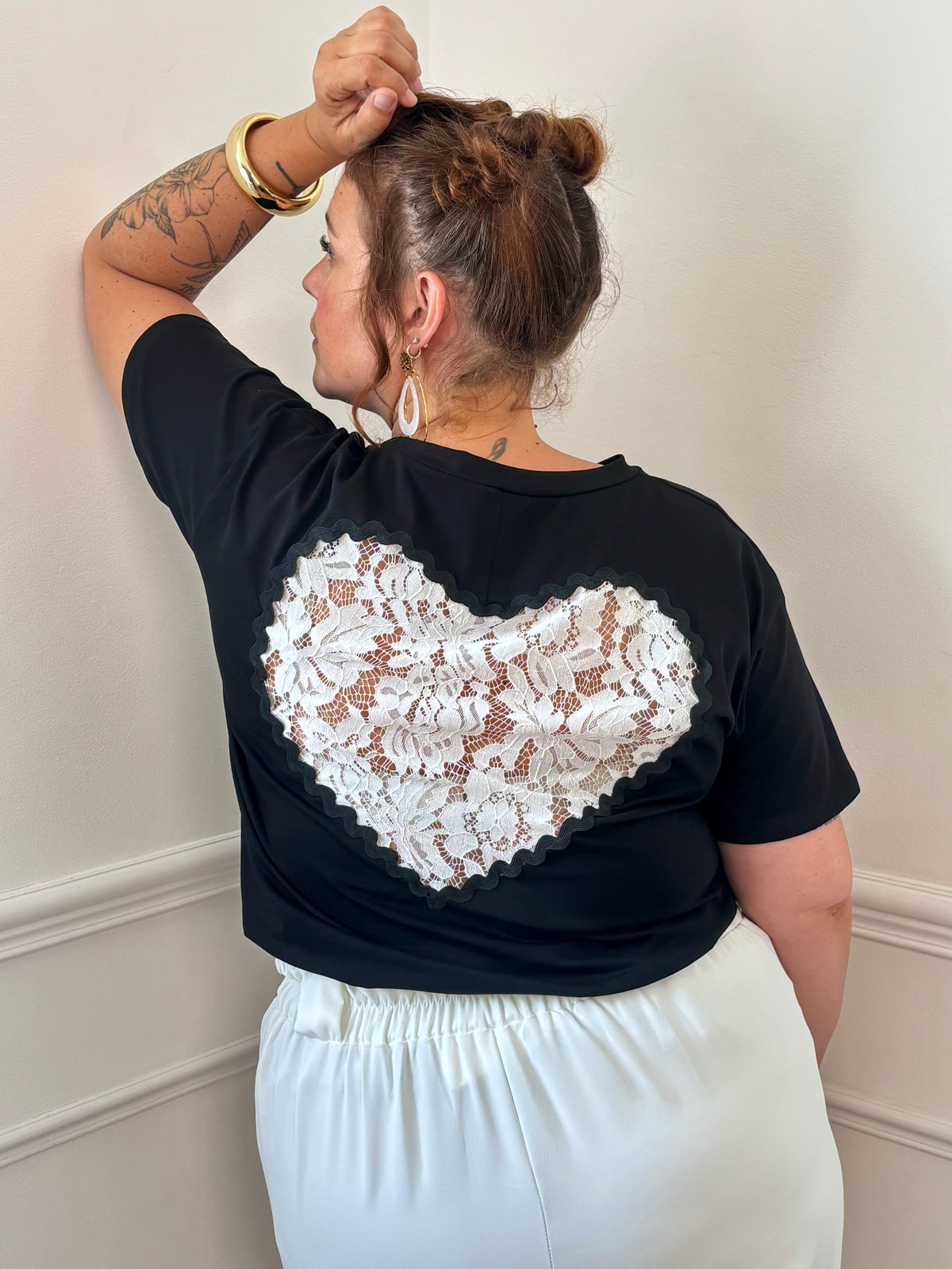 Ajoutez une touche de romantisme à vos tenues avec ce tee-shirt noir grande taille à la fois confortable et féminin. Doté d’un col rond et de manches courtes, il se distingue par son élégant empiècement en dentelle ajourée au dos, formant un délicat motif cœur. Confectionné dans une matière douce et légèrement extensible composée de 97% coton et 3% élasthanne, ce modèle noir et écru est idéal pour allier confort et style au quotidien.