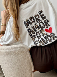 Top écru femme à manches courtes, parfait pour un look tendance et décontracté. Avec son col rond et son inscription effet léopard "More Amore Por Favor" à l’avant et au dos, il apporte une touche originale et moderne. Son détail cœur rouge ajoute une note féminine et stylée.