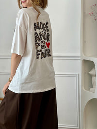 Top écru femme à manches courtes, parfait pour un look tendance et décontracté. Avec son col rond et son inscription effet léopard "More Amore Por Favor" à l’avant et au dos, il apporte une touche originale et moderne. Son détail cœur rouge ajoute une note féminine et stylée.