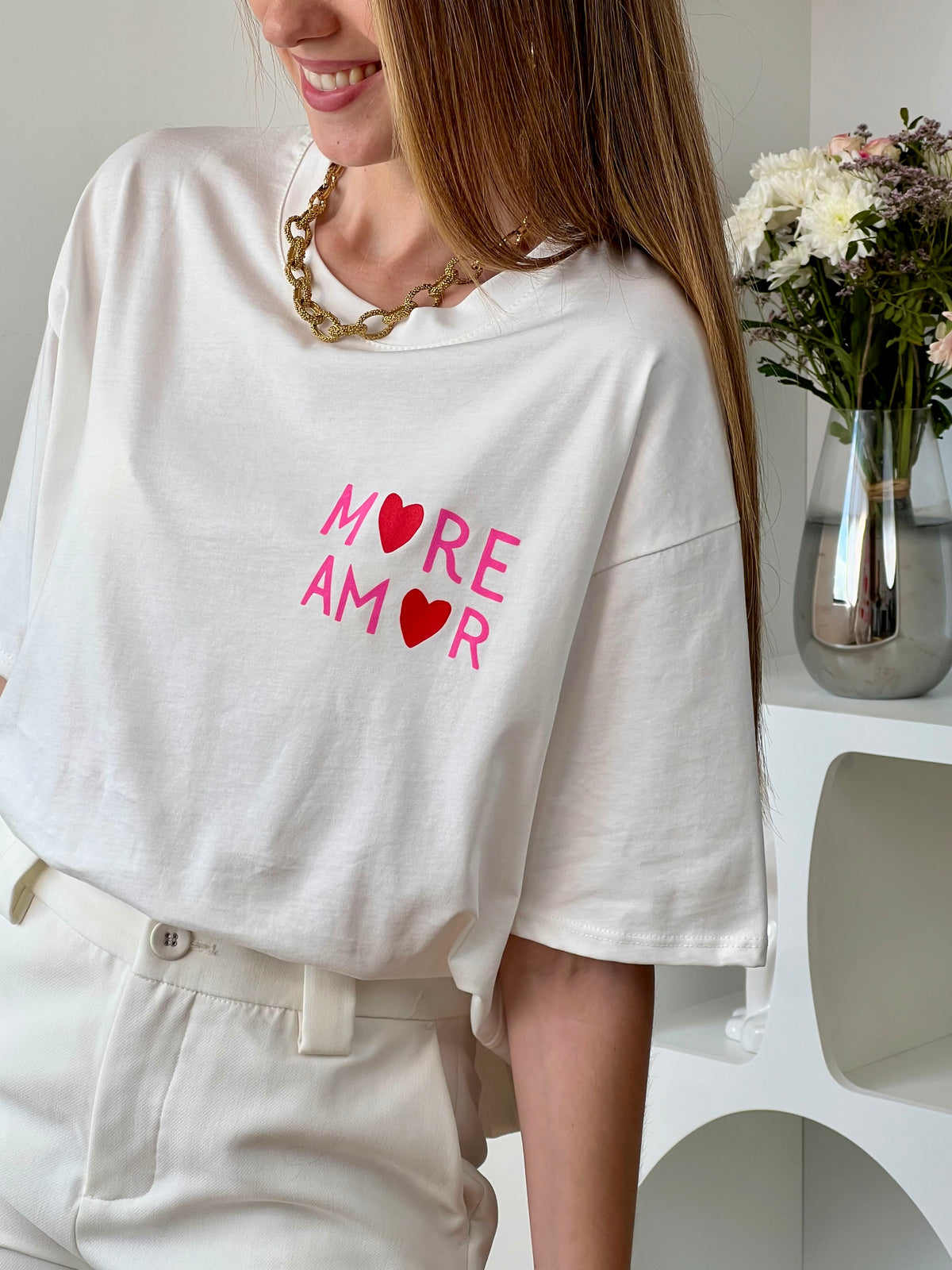 Top écru femme à manches courtes, parfait pour un look tendance et décontracté. Avec son col rond et son inscription rose "More Amore Por Favor" à l’avant et au dos, il apporte une touche originale et moderne. Son détail cœur rouge ajoute une note féminine et stylée.