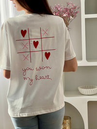 Craquez pour ce tee-shirt écru femme à manches courtes, à la fois doux et original. Doté d’un col rond et d’une inscription brodée “You won my heart” sur le devant et au dos, il est sublimé par des motifs de morpion avec cœurs et croix. Ses couleurs écru, rose et rouge apportent une touche romantique et tendance à votre tenue.