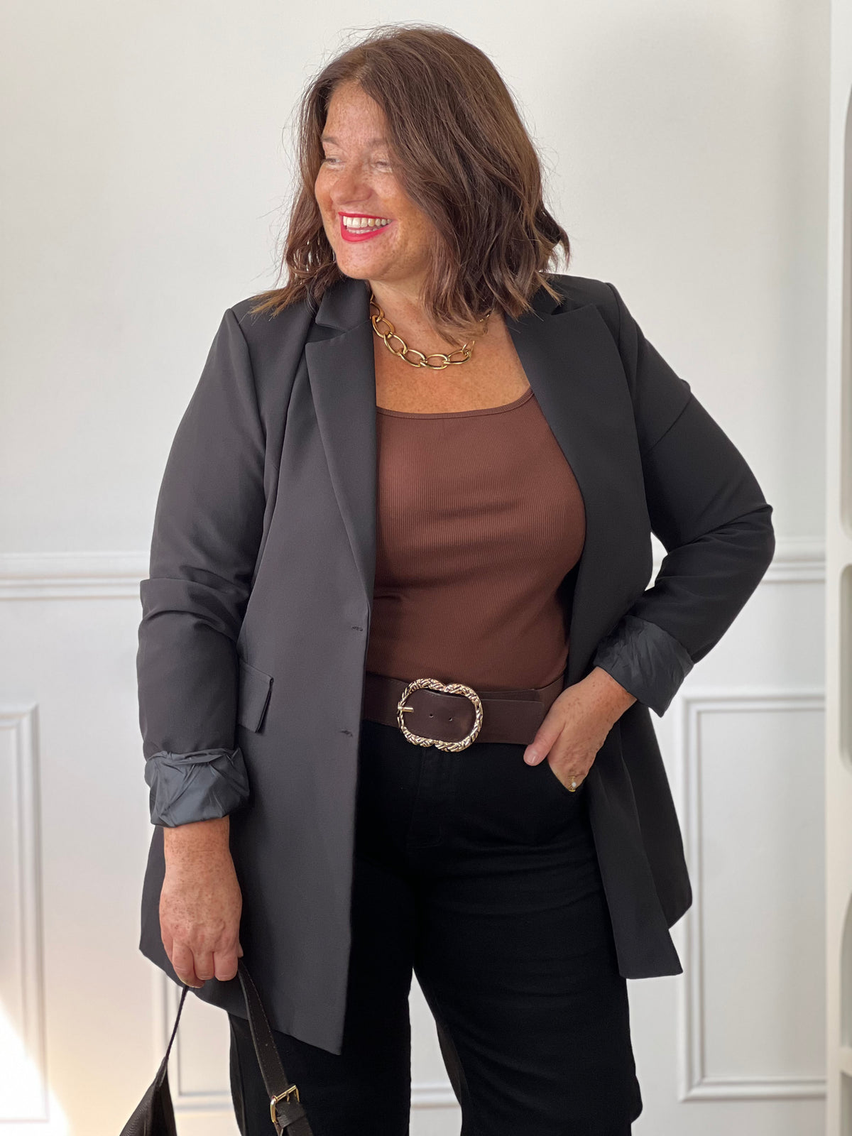 Top marron Alix à encolure carrée porté sous un blazer noir, avec un pantalon noir et une ceinture marron à boucle dorée.
