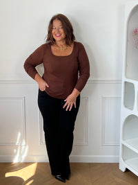 Top marron Alix grande taille porté de face avec un pantalon noir, montrant l’encolure carrée et les manches longues.