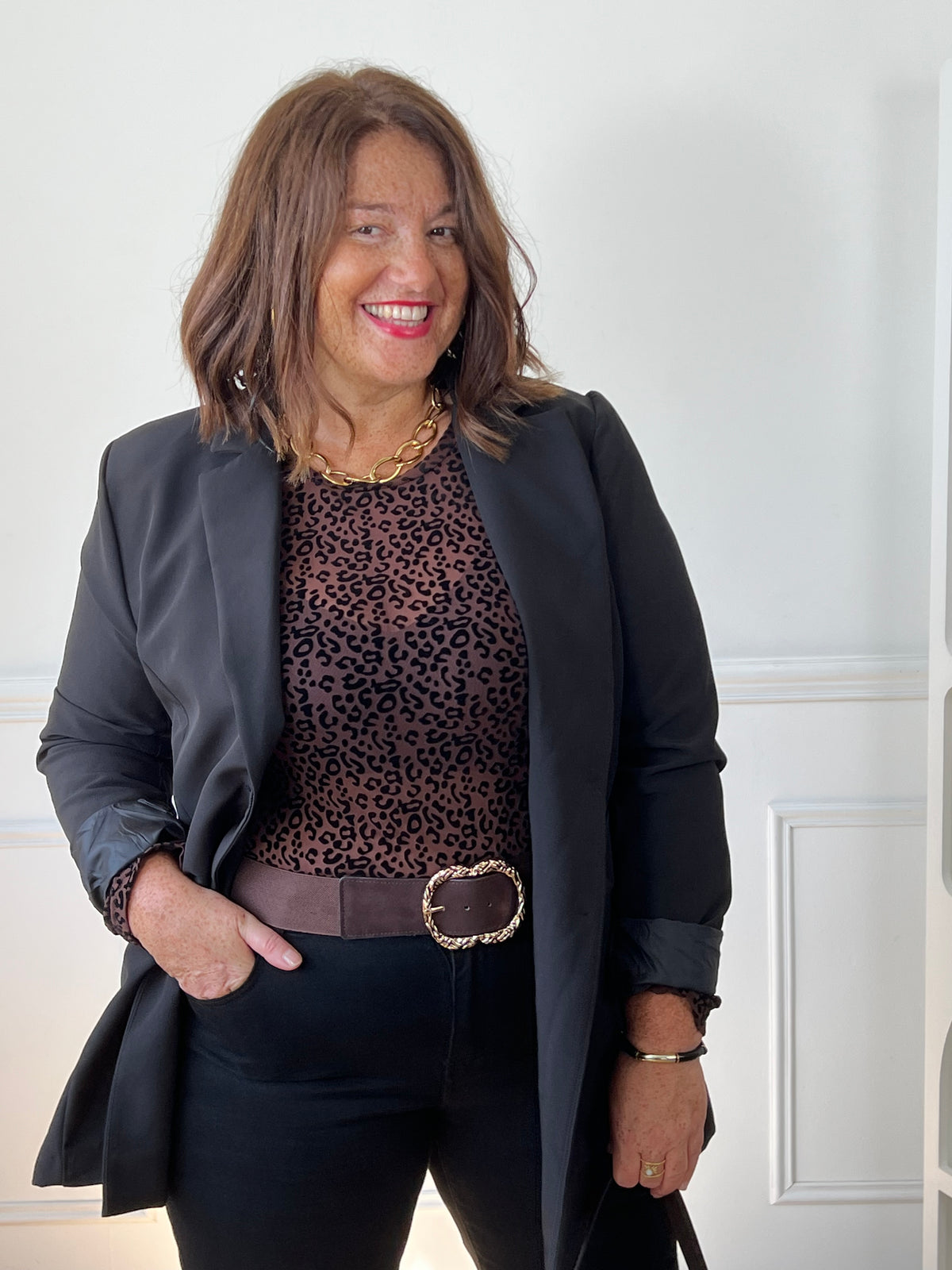 Top léopard Zeline grande taille porté sous un blazer noir, avec un pantalon noir et une ceinture marron à boucle dorée.