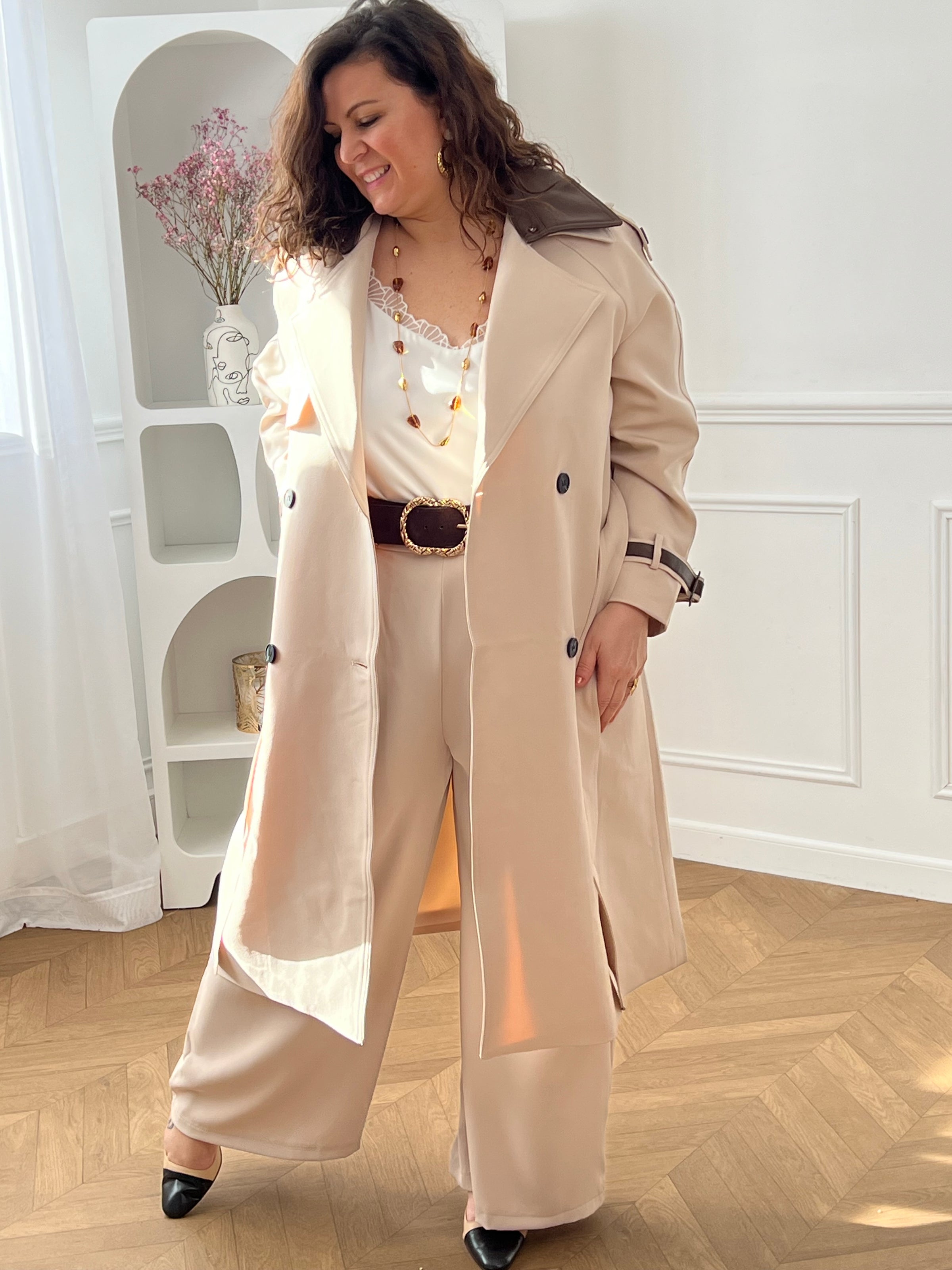Découvrez le manteau long Elior beige et marron femme, un élégant trench intemporel. Il dispose de liens de serrage aux poignets, de passants avec ceinture amovible pour marquer la taille et de deux poches latérales pratiques. Son double col à revers est rehaussé de détails en simili cuir marron amovibles au col et aux poignets. Une pièce chic et raffinée pour la mi-saison.