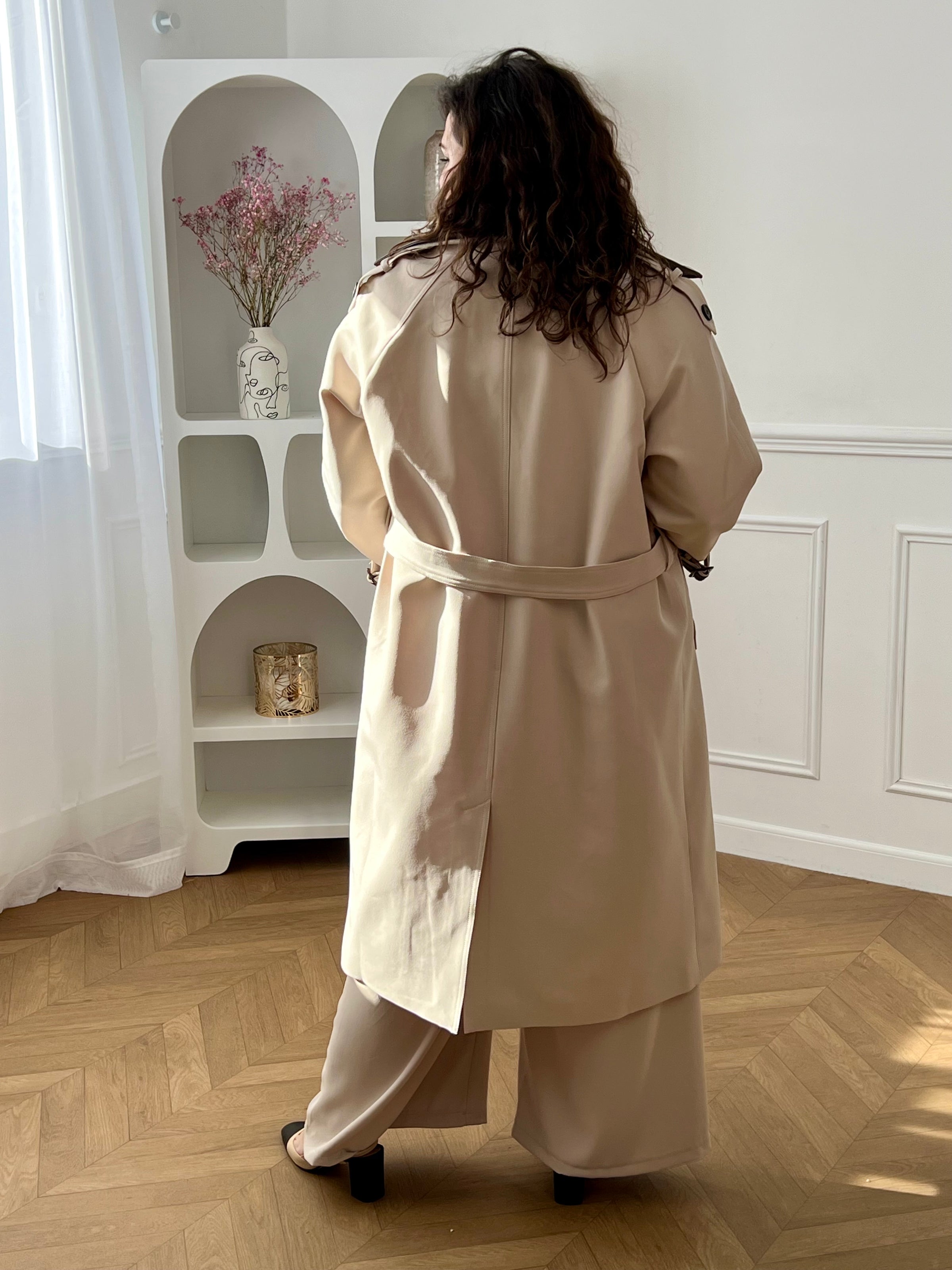 Découvrez le manteau long Elior beige et marron femme, un élégant trench intemporel. Il dispose de liens de serrage aux poignets, de passants avec ceinture amovible pour marquer la taille et de deux poches latérales pratiques. Son double col à revers est rehaussé de détails en simili cuir marron amovibles au col et aux poignets. Une pièce chic et raffinée pour la mi-saison.