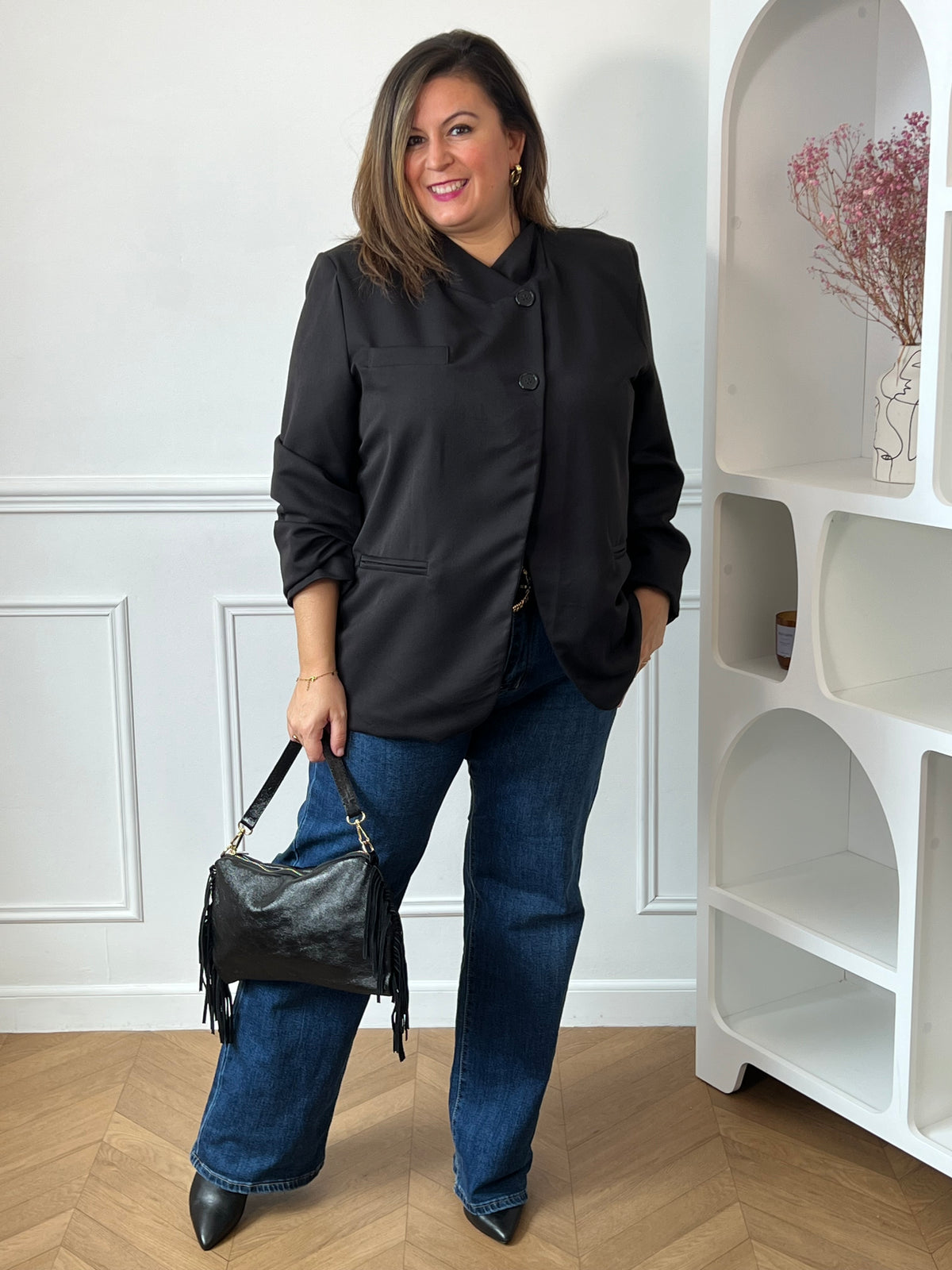 Veste noire Loen grande taille portée fermée avec un jean bleu et un sac noir à franges, vue de face en pied.