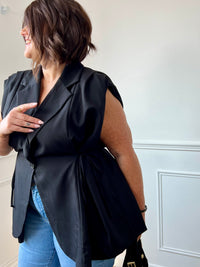 Veste noire cintrée grande taille femme, idéale pour structurer votre silhouette avec élégance. Sans manches, elle se distingue par ses épaules froncées et son col à revers pour une touche chic. Dotée de liens à nouer sur les côtés pour ajuster la taille et d’un bouton sur le devant, elle allie style et praticité. Entièrement doublée, cette veste noire est parfaite pour compléter vos tenues avec modernité.