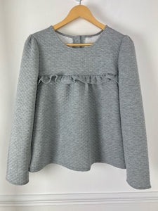 BLOUSE GRISE EFFET MATELASSE FEMME Blouse Manches longues Col rond Couleur : gris Effet matelassé  Volant sur le devant Détail fermetures avec gros boutons à l'arrière